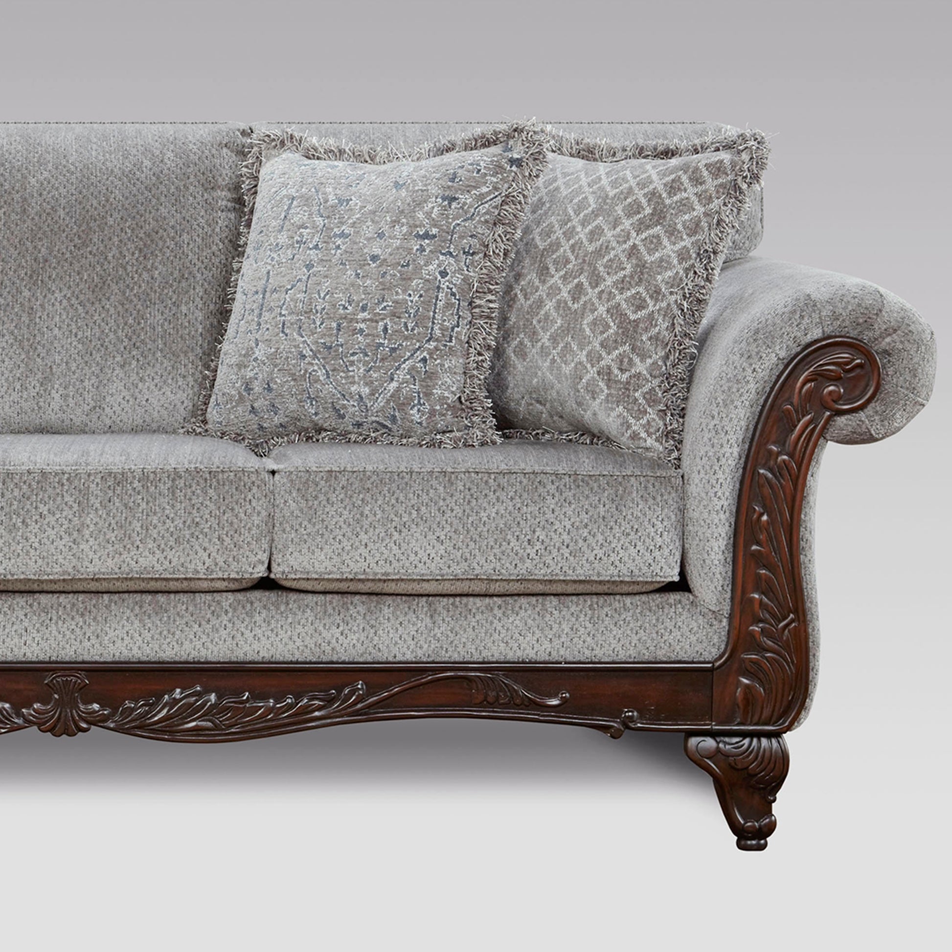 Grey fabric sofa with ornate carved wood armrest and fringe accent pillows