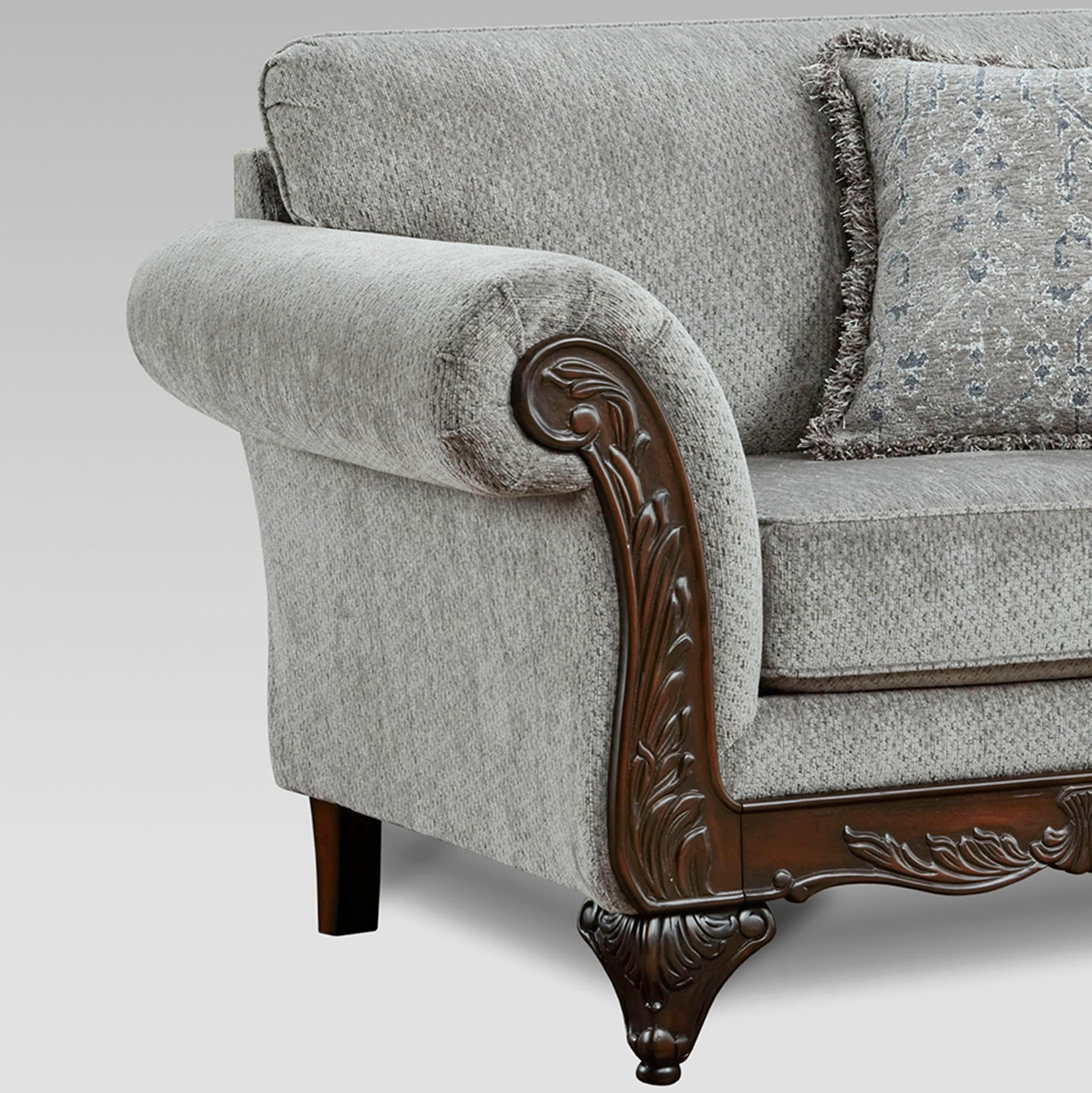Closeup of a grey upholstered sofa with ornate dark wood armrest detailing and a patterned pillow