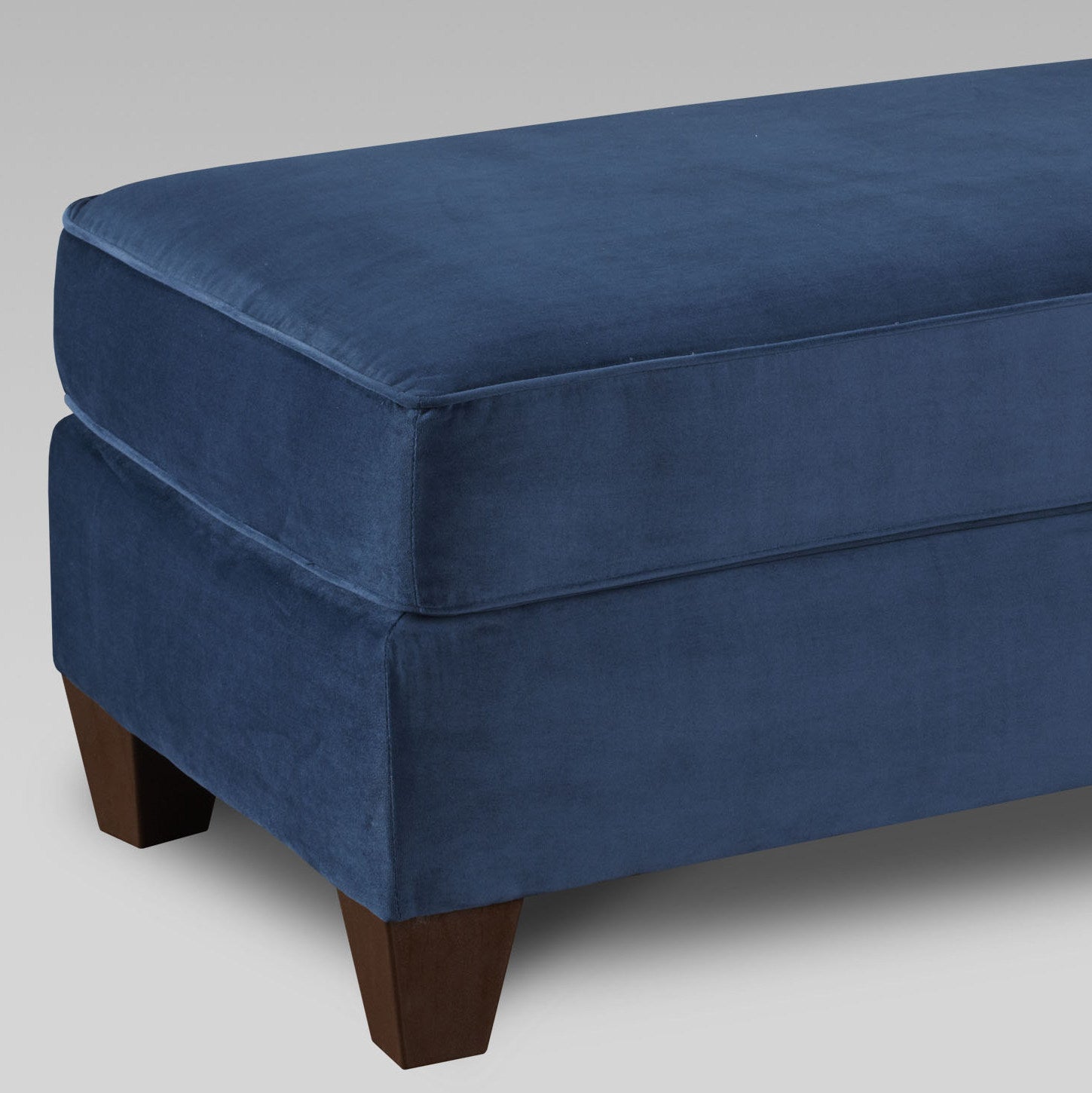 Deep blue velvet ottoman with cushioned top and dark wood legs