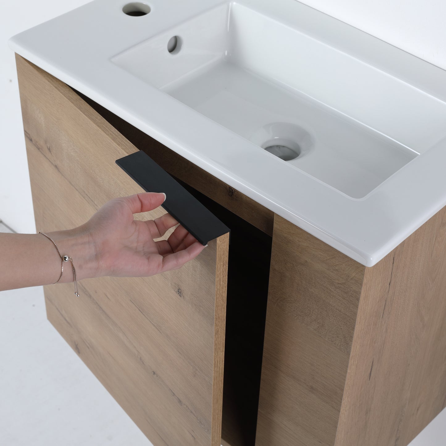 Closeup of a hand opening a modern oak vanity cabinet door with a sleek black handle