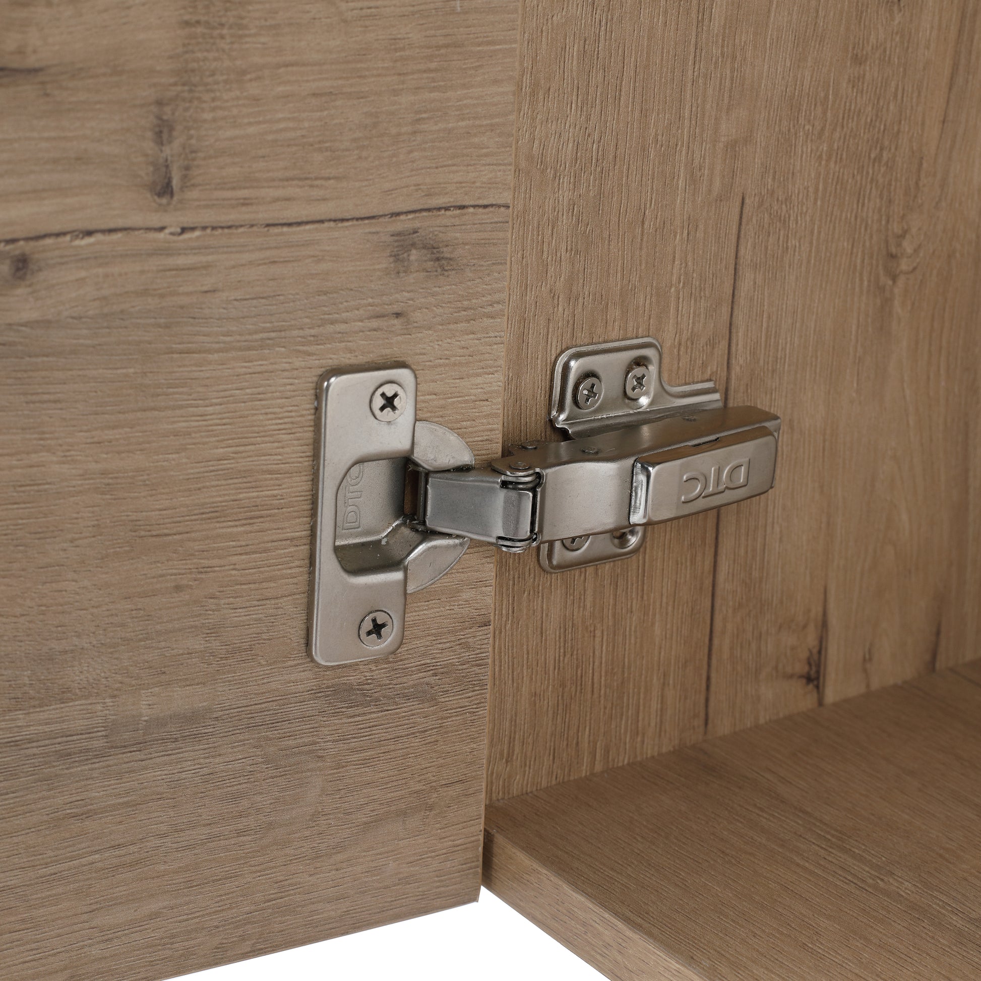 Closeup of a brushed nickel cabinet hinge attached to a light wood grain door
