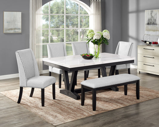 Gray upholstered dining chairs with nailhead trim surrounding a faux marble top dining table with dark wood legs