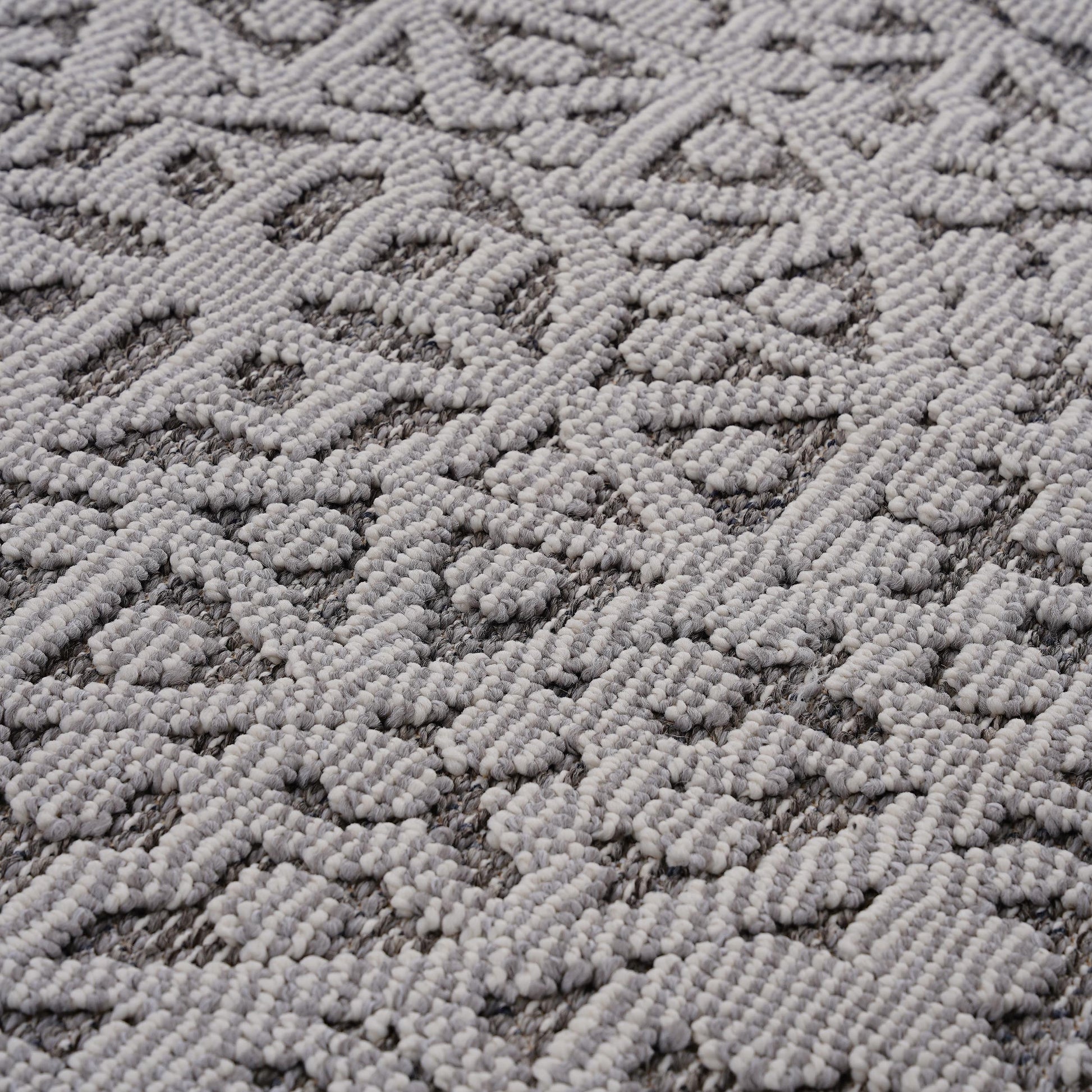 Closeup of a grey and white textured area rug with a geometric diamond pattern