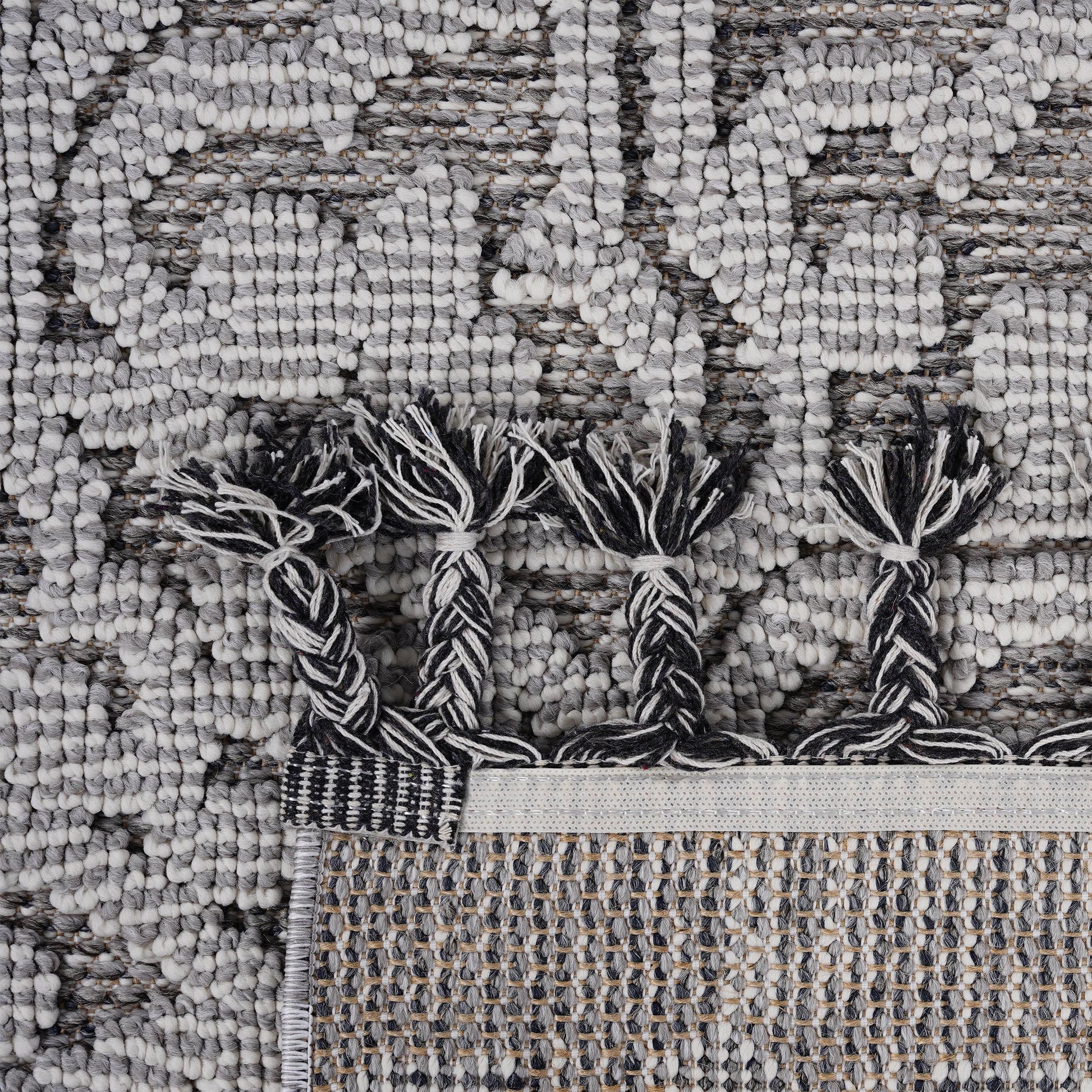 Closeup of a grey and white textured rug with black and white braided tassels for a bohemian look