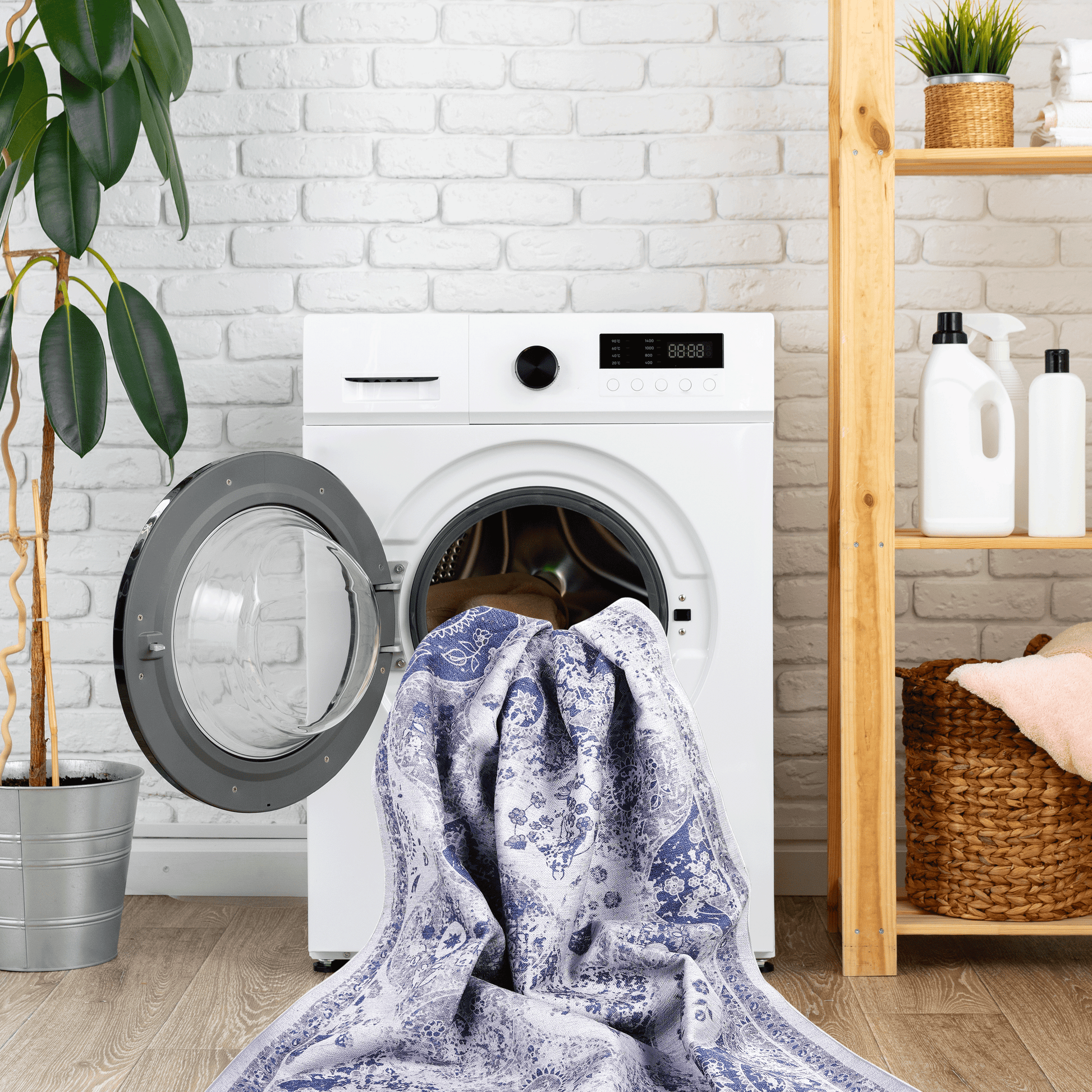 Blue and white ornate patterned rug being loaded into a white washing machine for cleaning