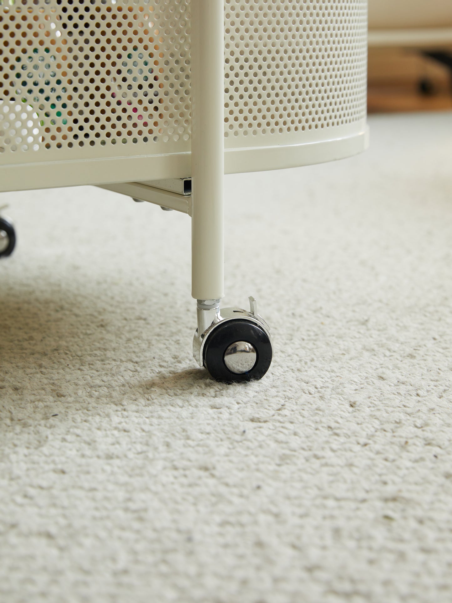 Cream perforated metal storage cart with swivel casters on shag carpet