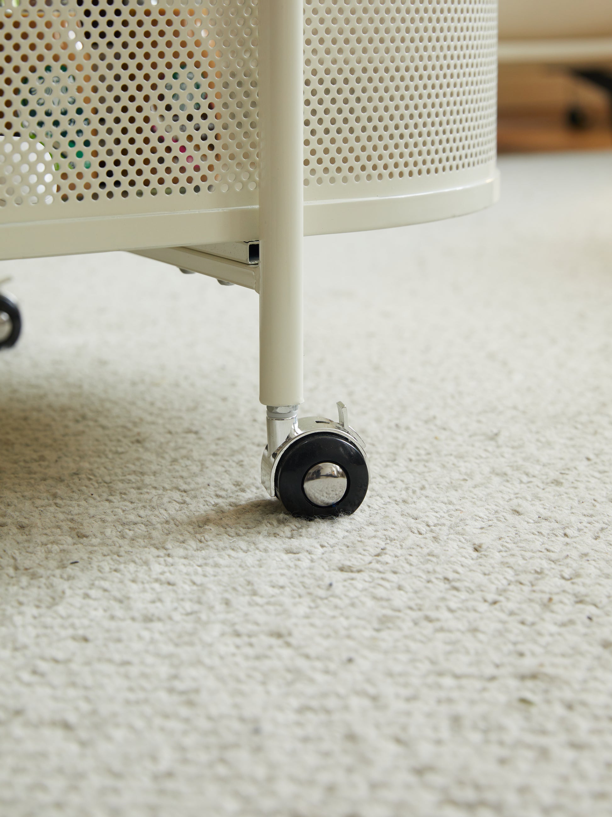 Cream perforated metal storage cart with swivel casters on shag carpet