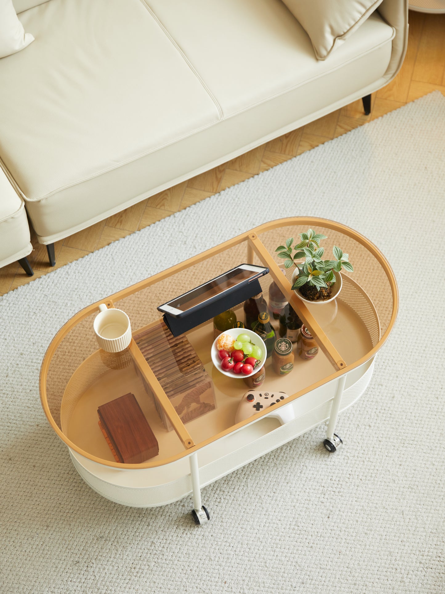 Oval rolling coffee table with glass top featuring fruit drinks and a tablet