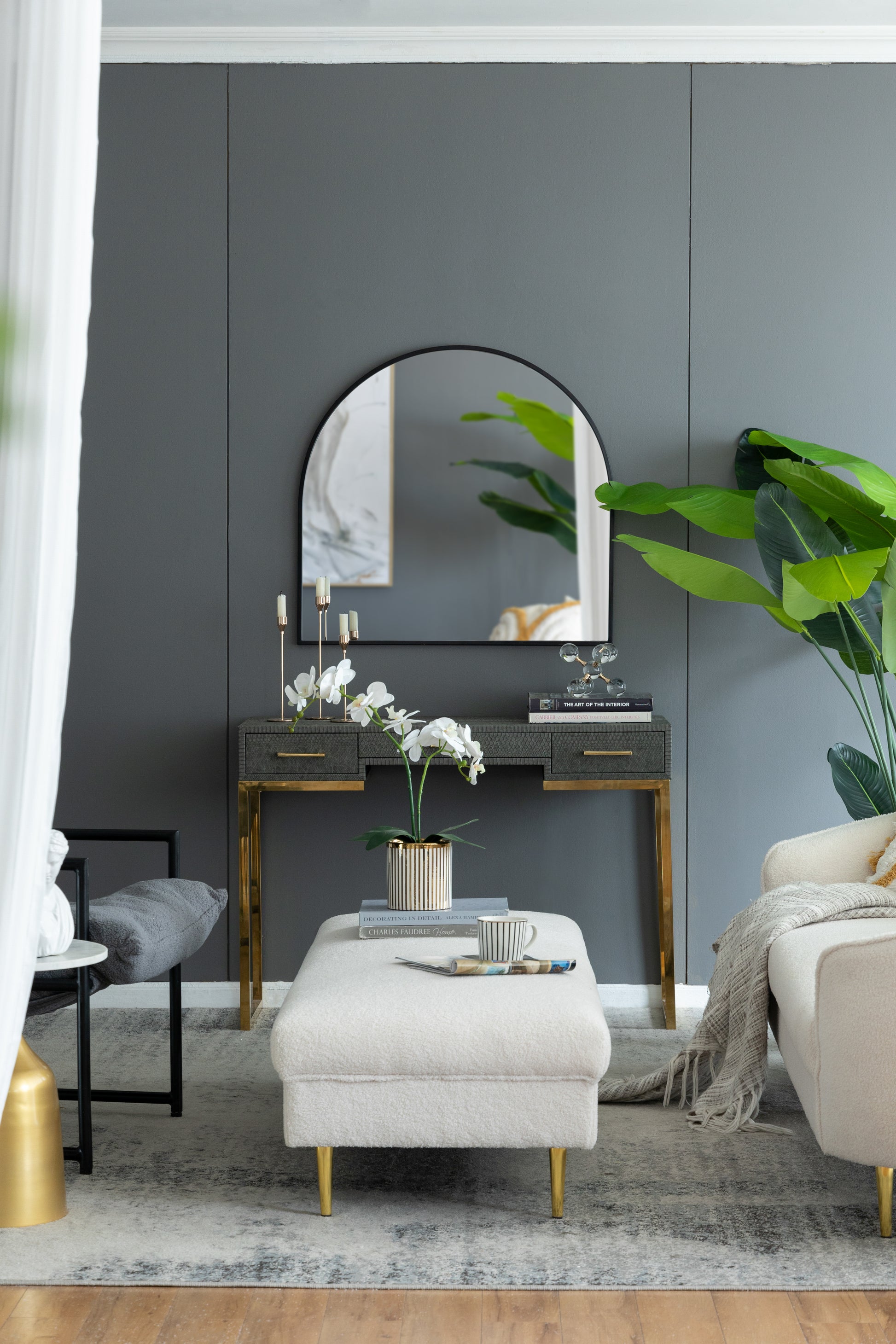 Elegant grey textured console table with gold legs and brass drawer pulls featuring a large arched mirror above