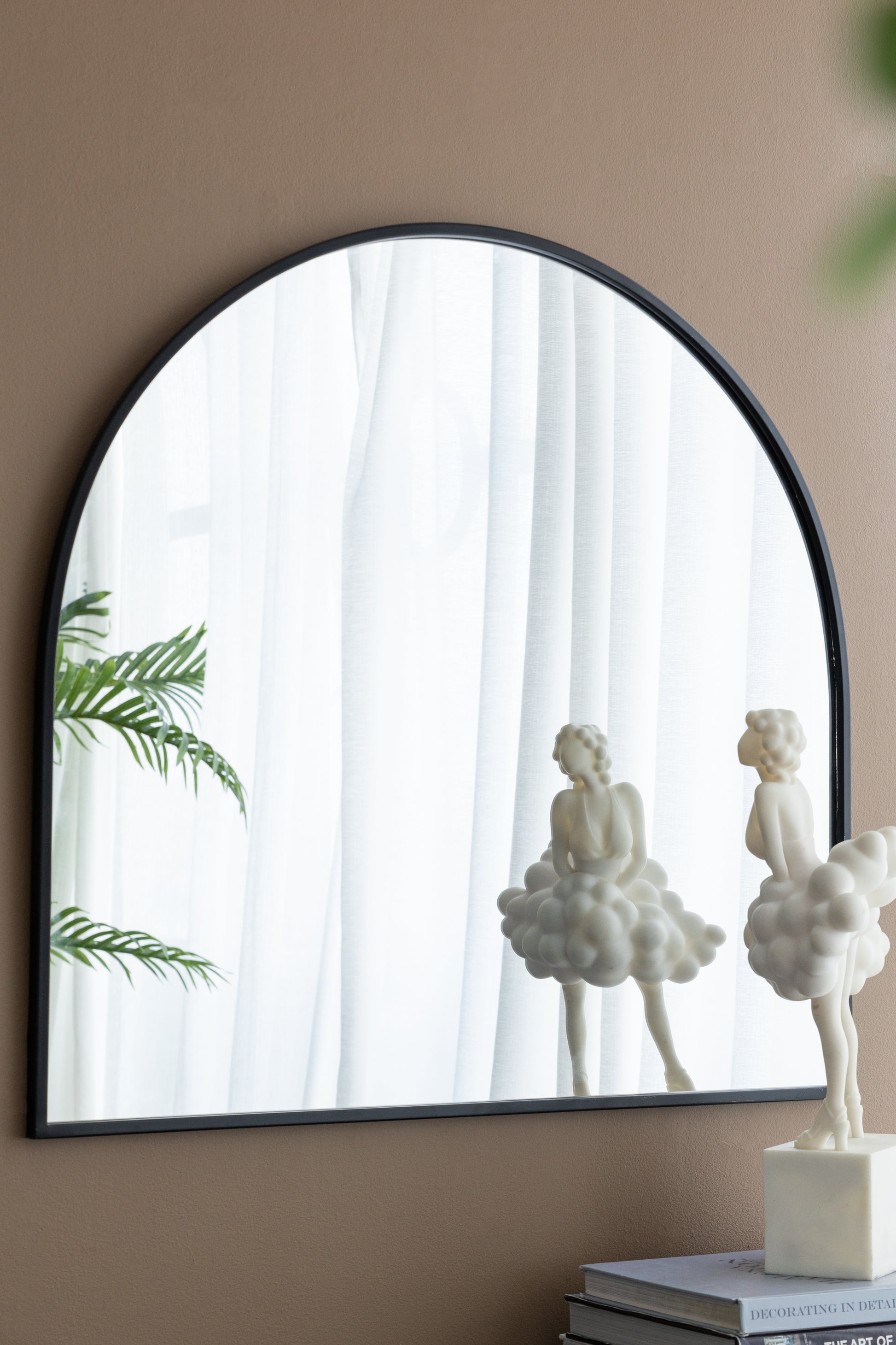 Black arched metal framed mirror with reflective surface and plant reflection