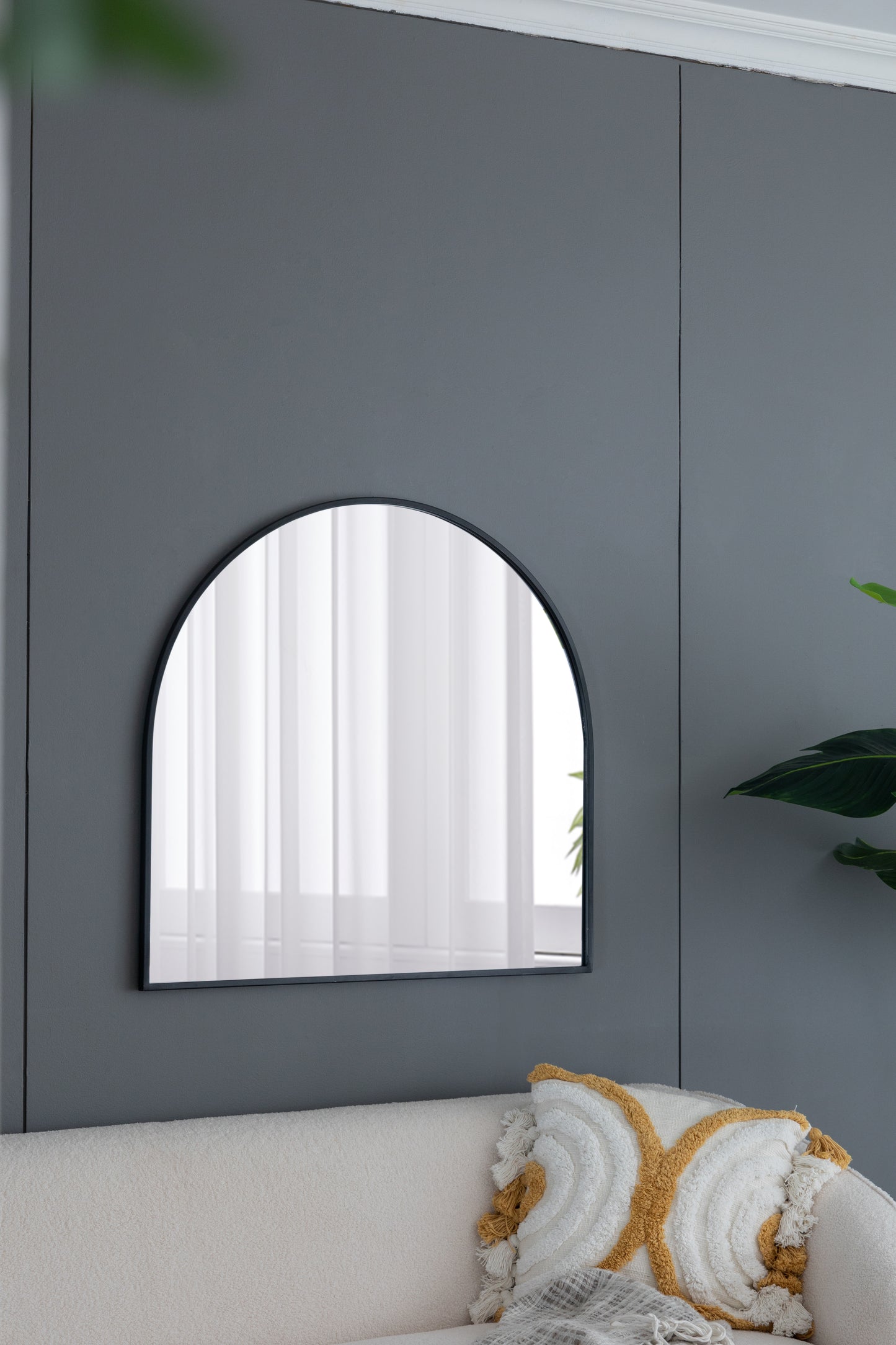 Arched black metal frame mirror reflecting sheer white curtains ideal for modern entryway