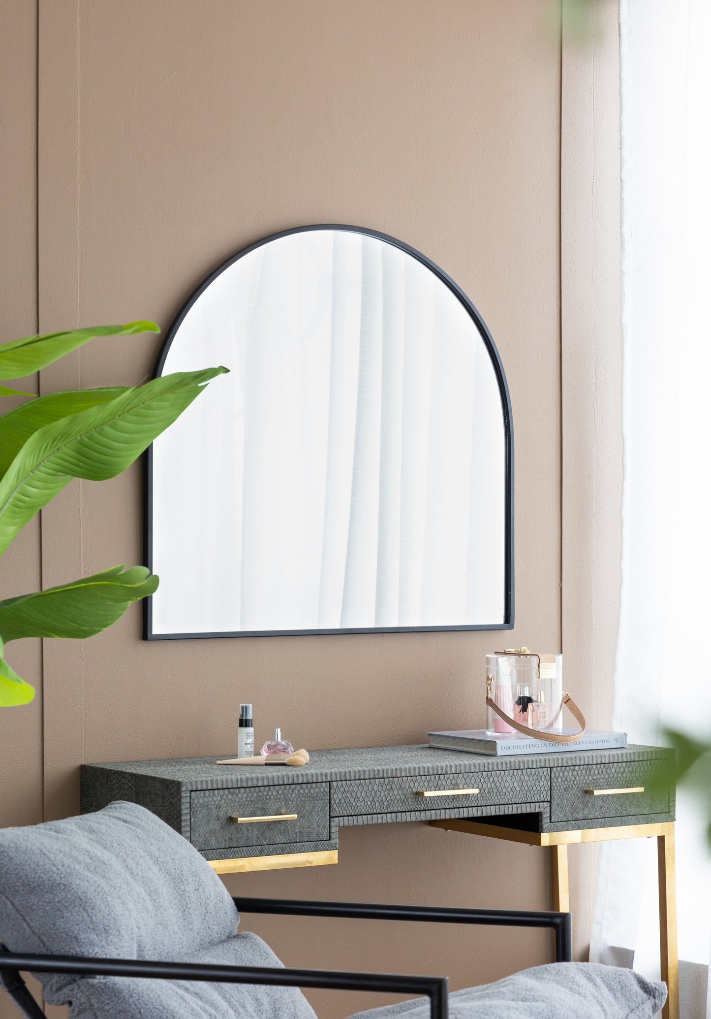 Modern arched black metal frame wall mirror above a grey embossed vanity desk with gold accents