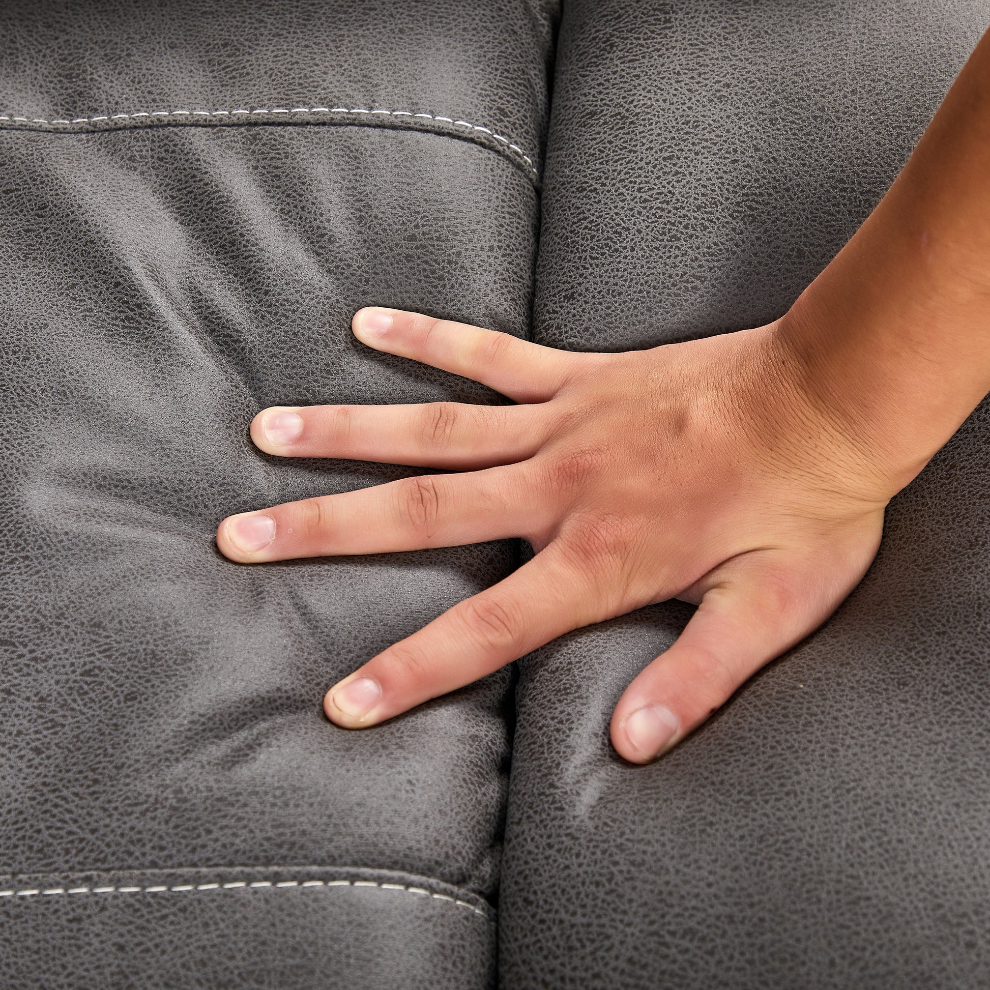 Closeup of a hand touching dark grey textured faux leather couch material