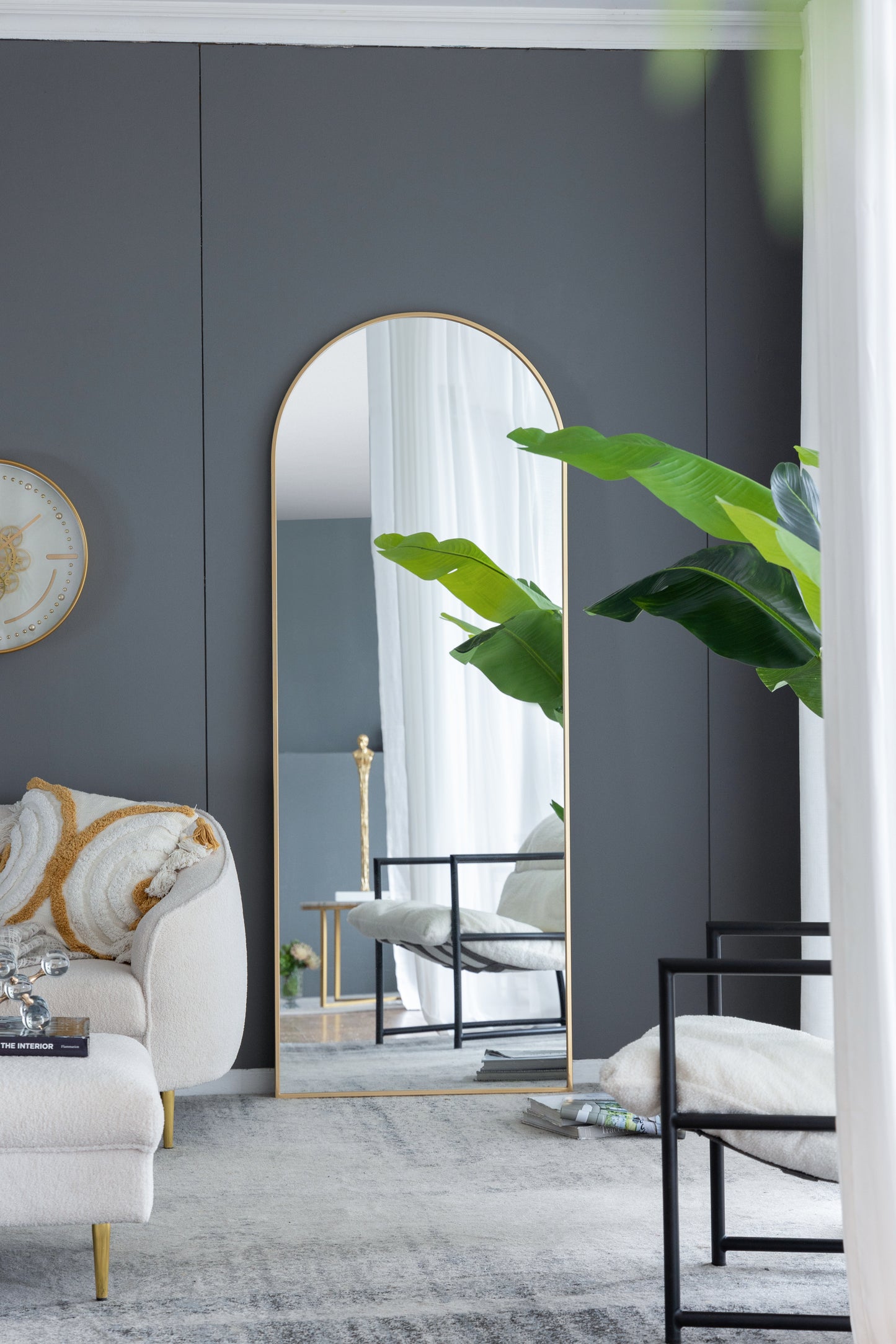 Tall arched gold mirror reflecting a modern living room with plants and furniture