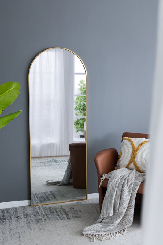Tall arched gold floor mirror leaning against gray wall modern home decor
