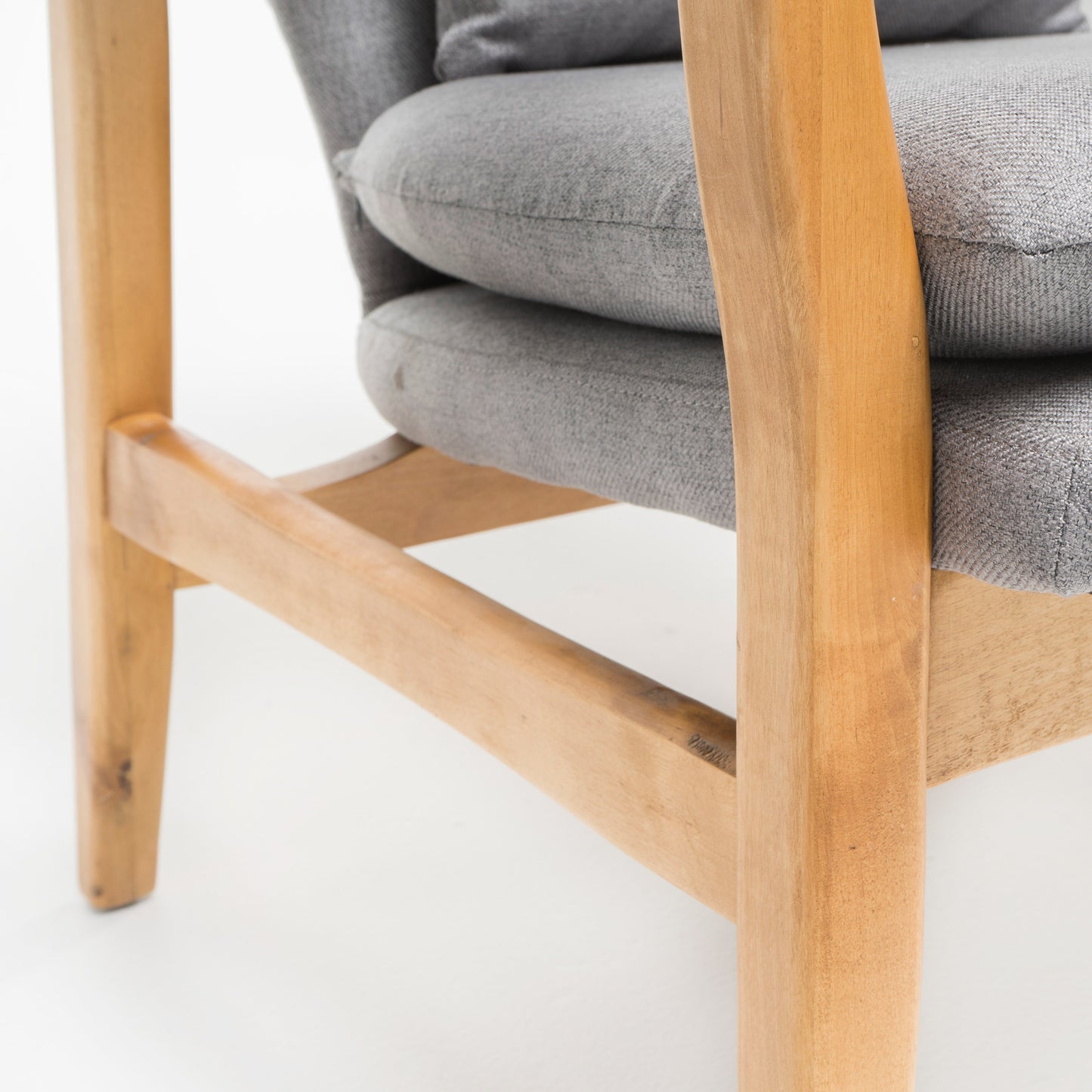 Closeup of textured grey fabric armchair cushion with natural wood frame details