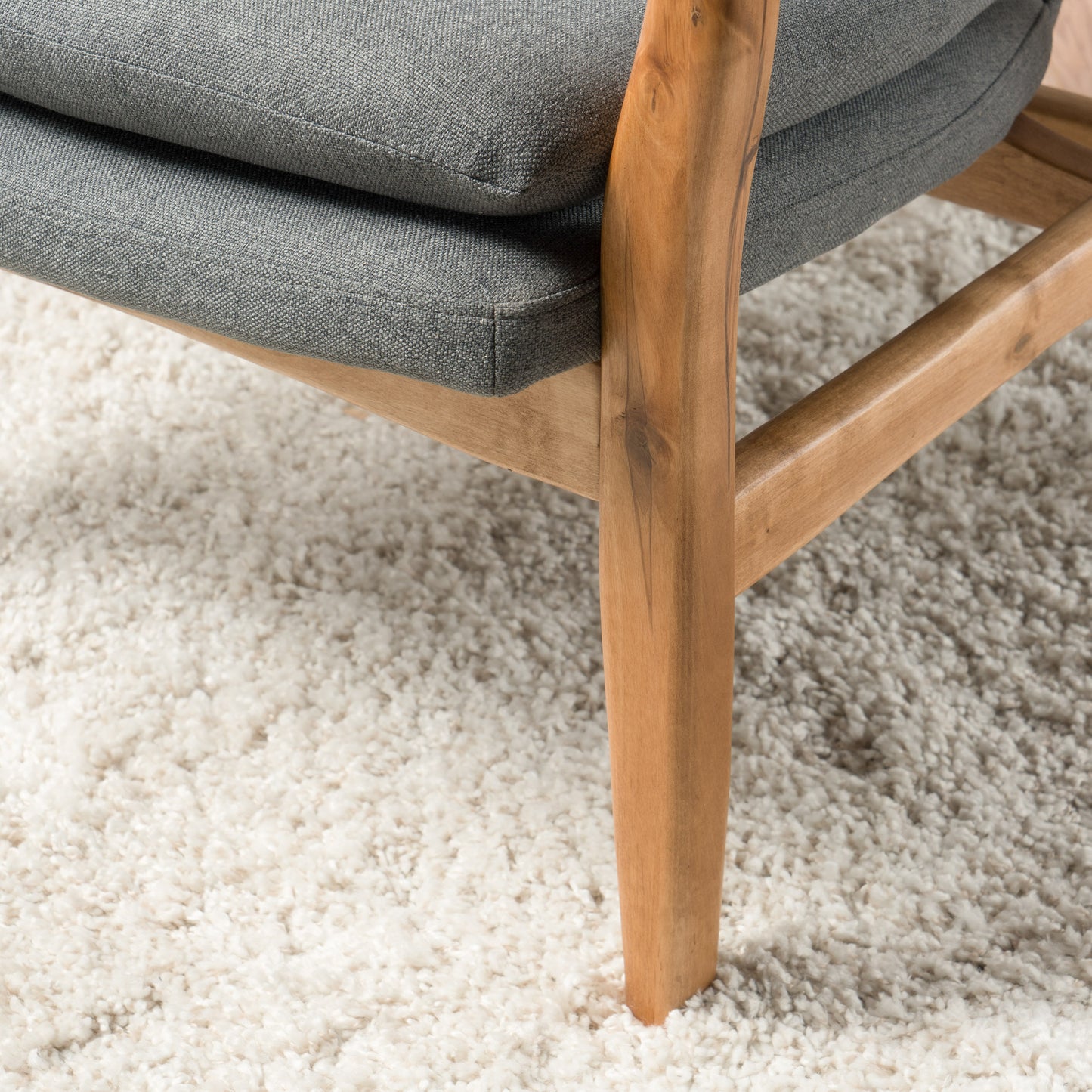 Closeup of a textured grey fabric armchair cushion and wooden frame on a white shag rug