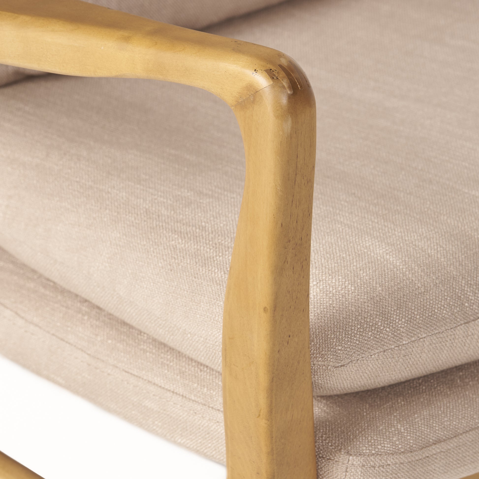 Closeup of a light beige fabric chair with a smooth wooden armrest