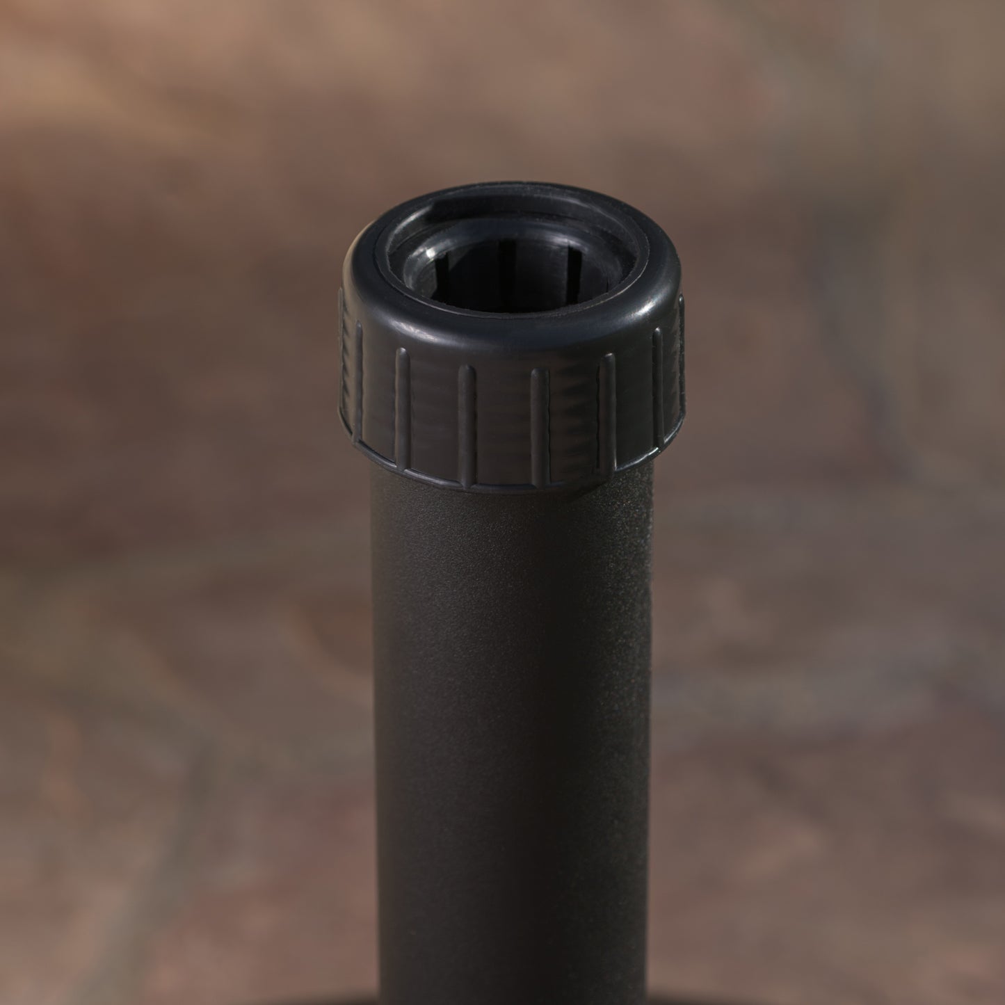 Closeup of a black textured umbrella pole with a black plastic finial for outdoor use
