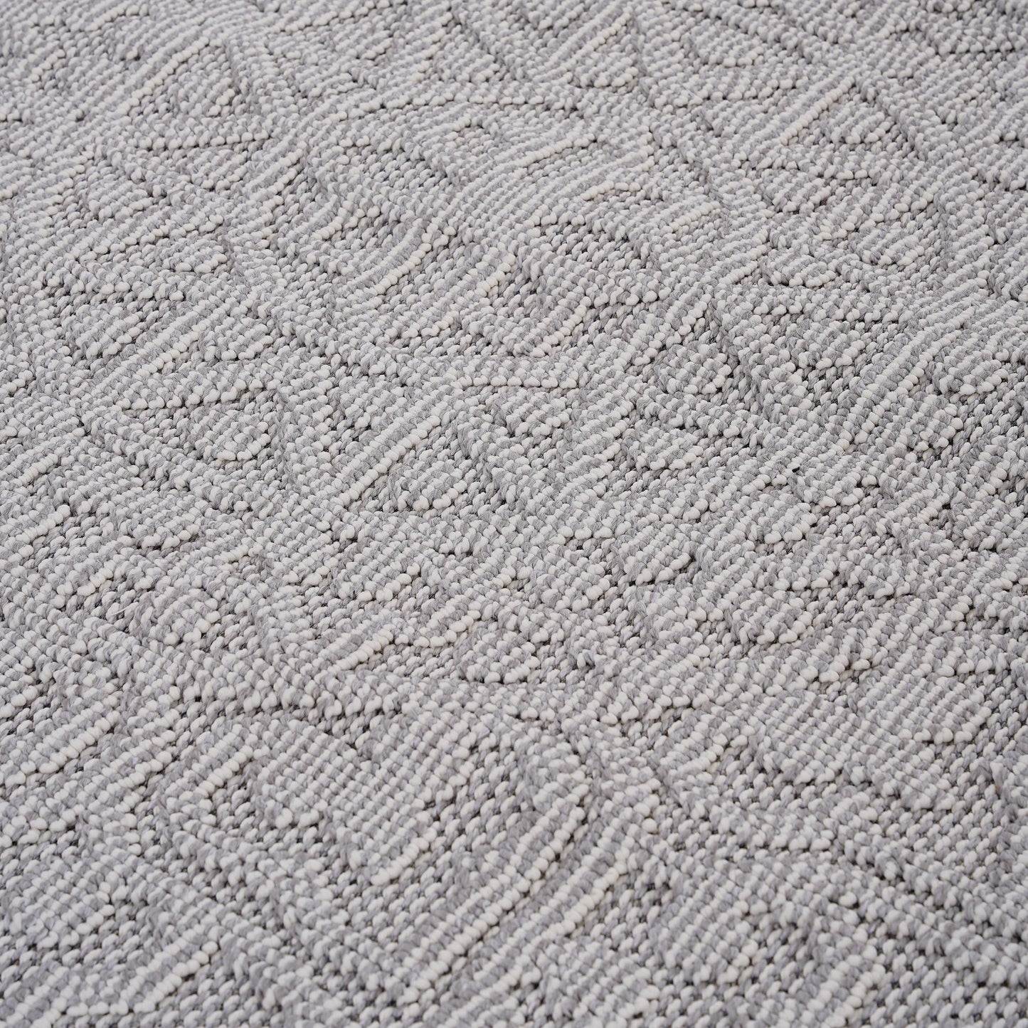 Closeup texture of a grey and white woven rug with a chevron pattern