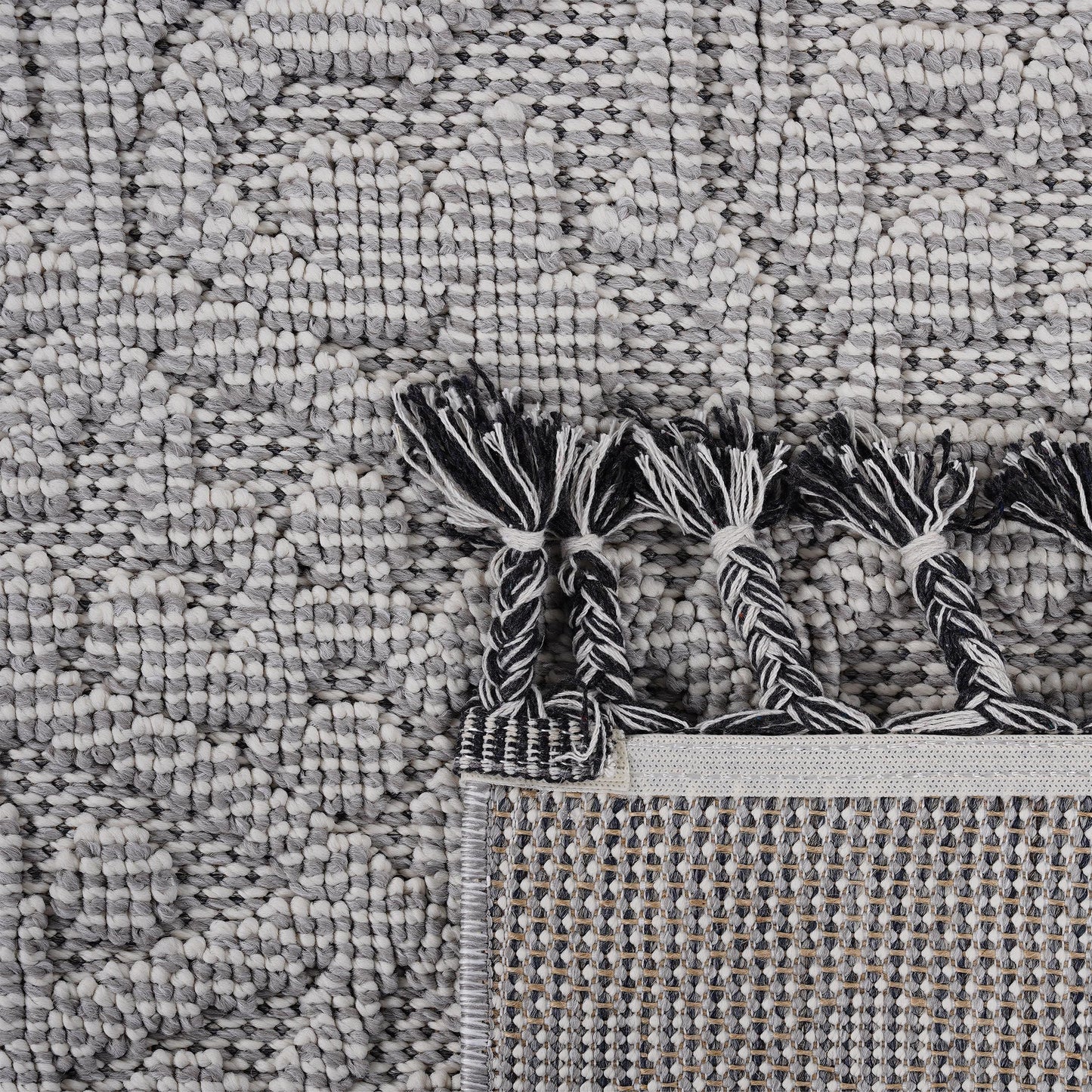 Textured grey and white patterned rug with braided tassels and woven backing
