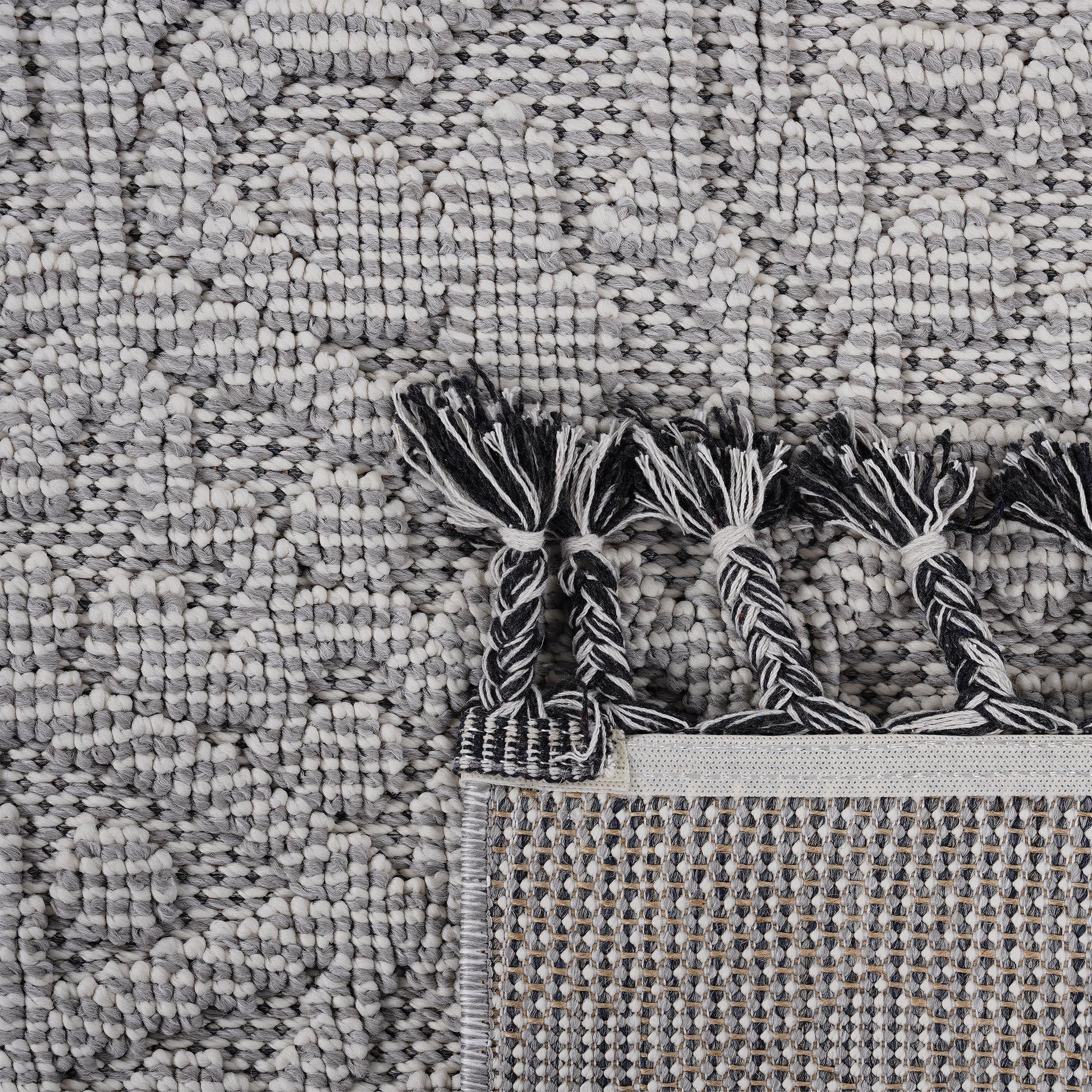 Textured grey and white patterned rug with braided tassels and woven backing