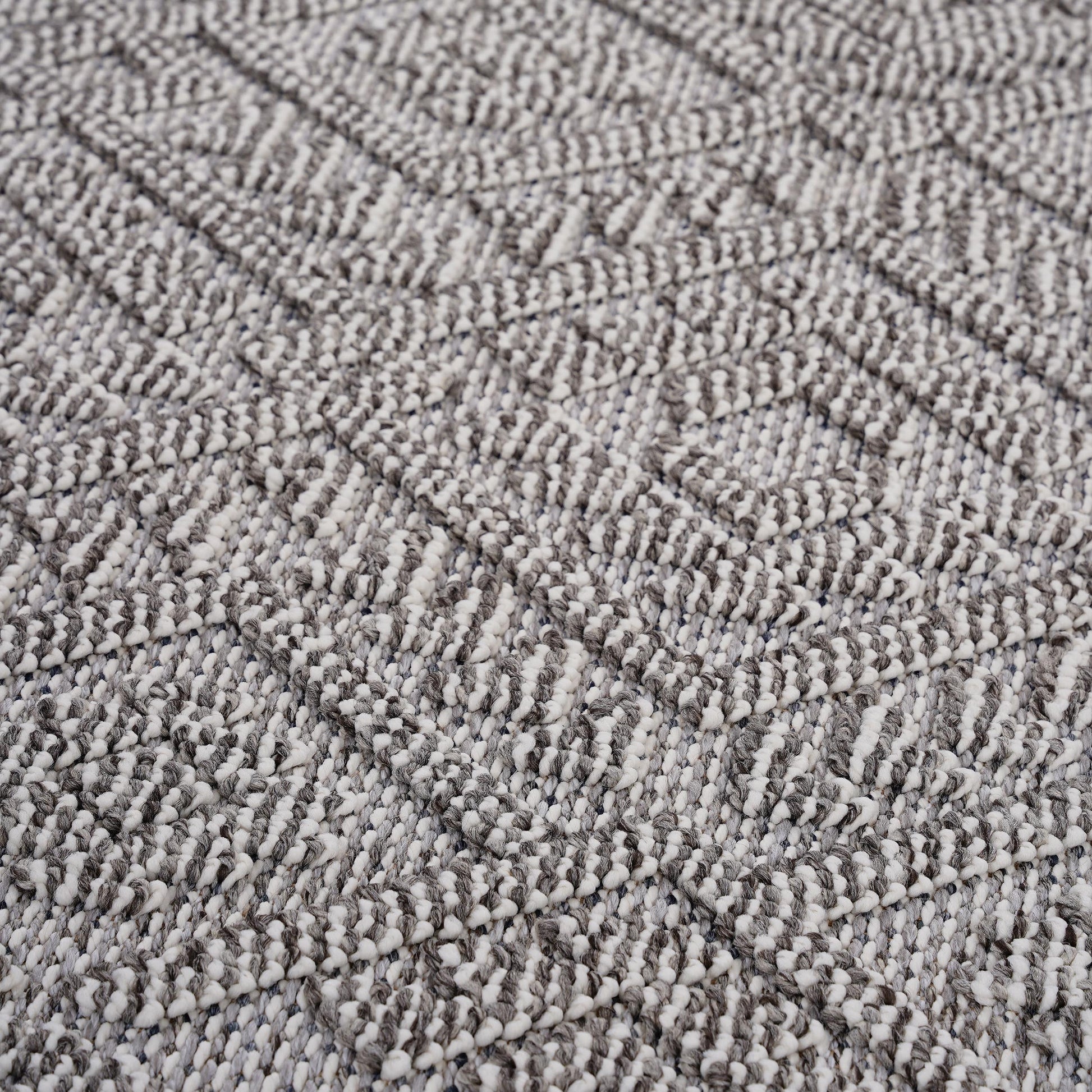 Closeup of a textured grey and white braided rug with a diamond pattern