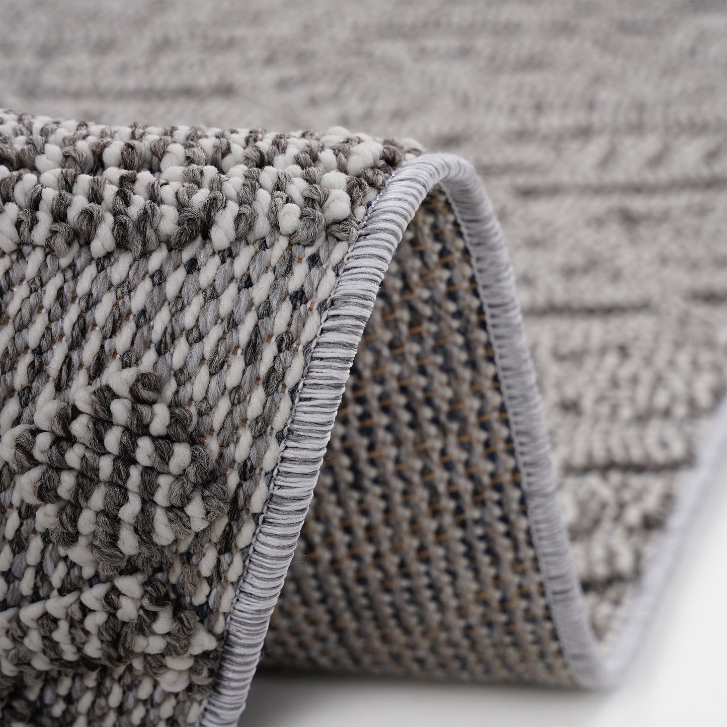 Closeup of a textured grey and white woven rug with a rolled edge and detailed tufting