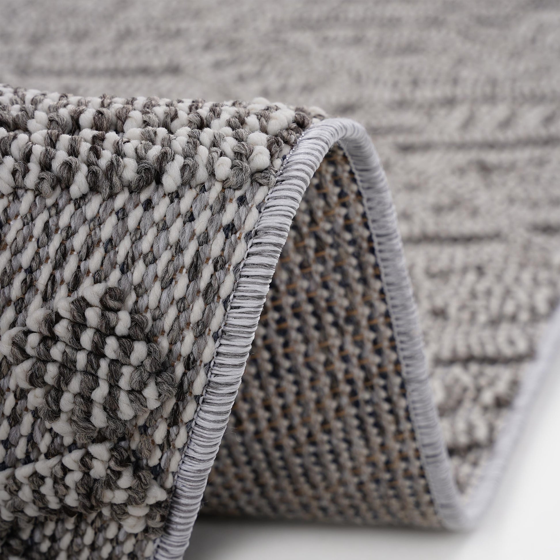 Closeup of a textured grey and white woven rug with a rolled edge and detailed tufting