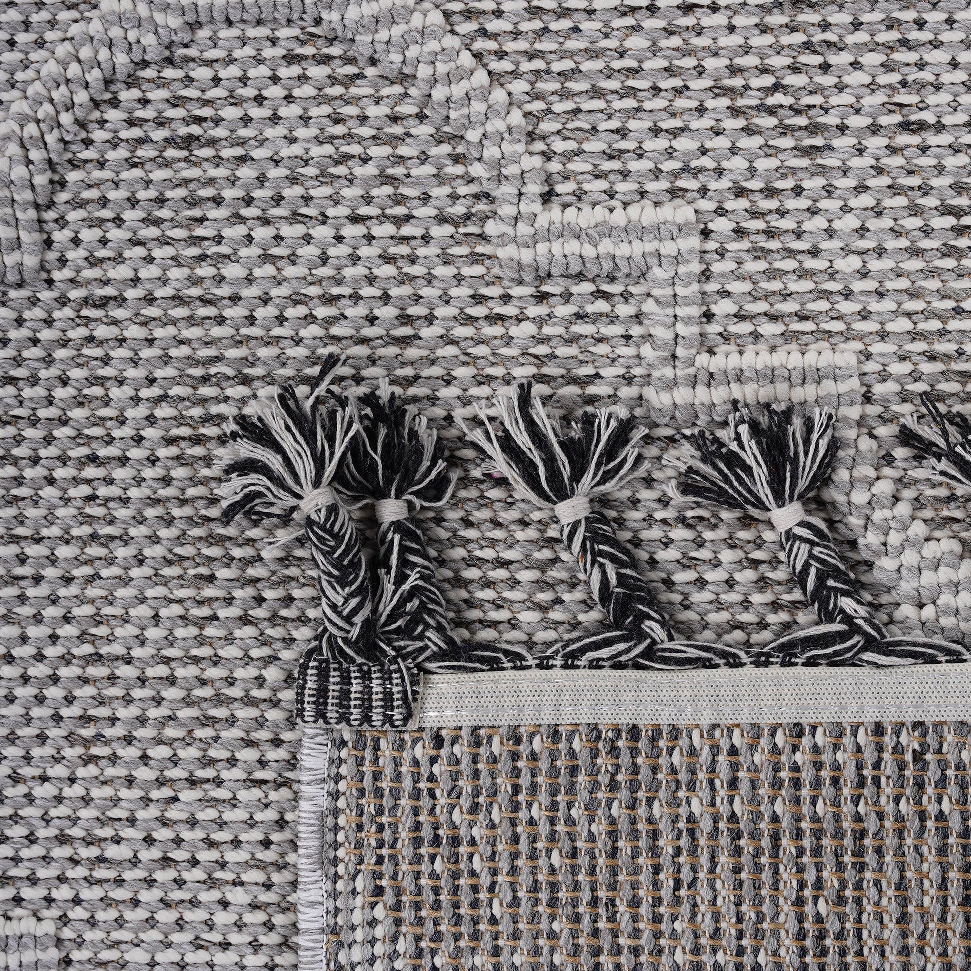 Closeup texture of a grey and white woven rug with black and white tassels