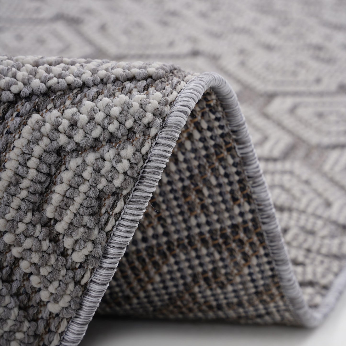 Closeup of a textured grey and white area rug with a diamond pattern and serged edge