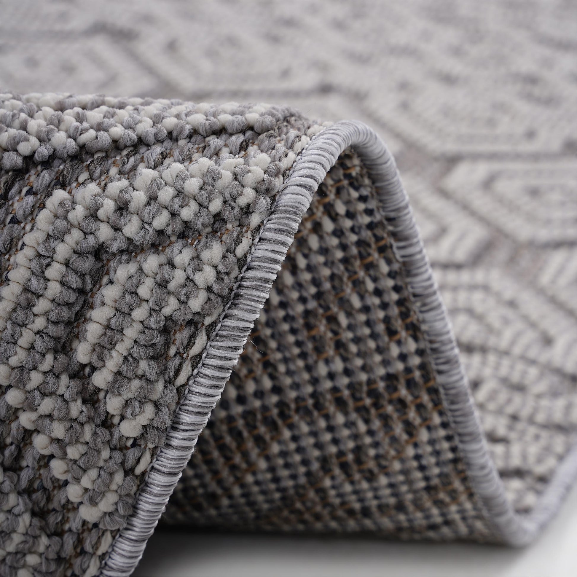 Closeup of a textured grey and white area rug with a diamond pattern and serged edge