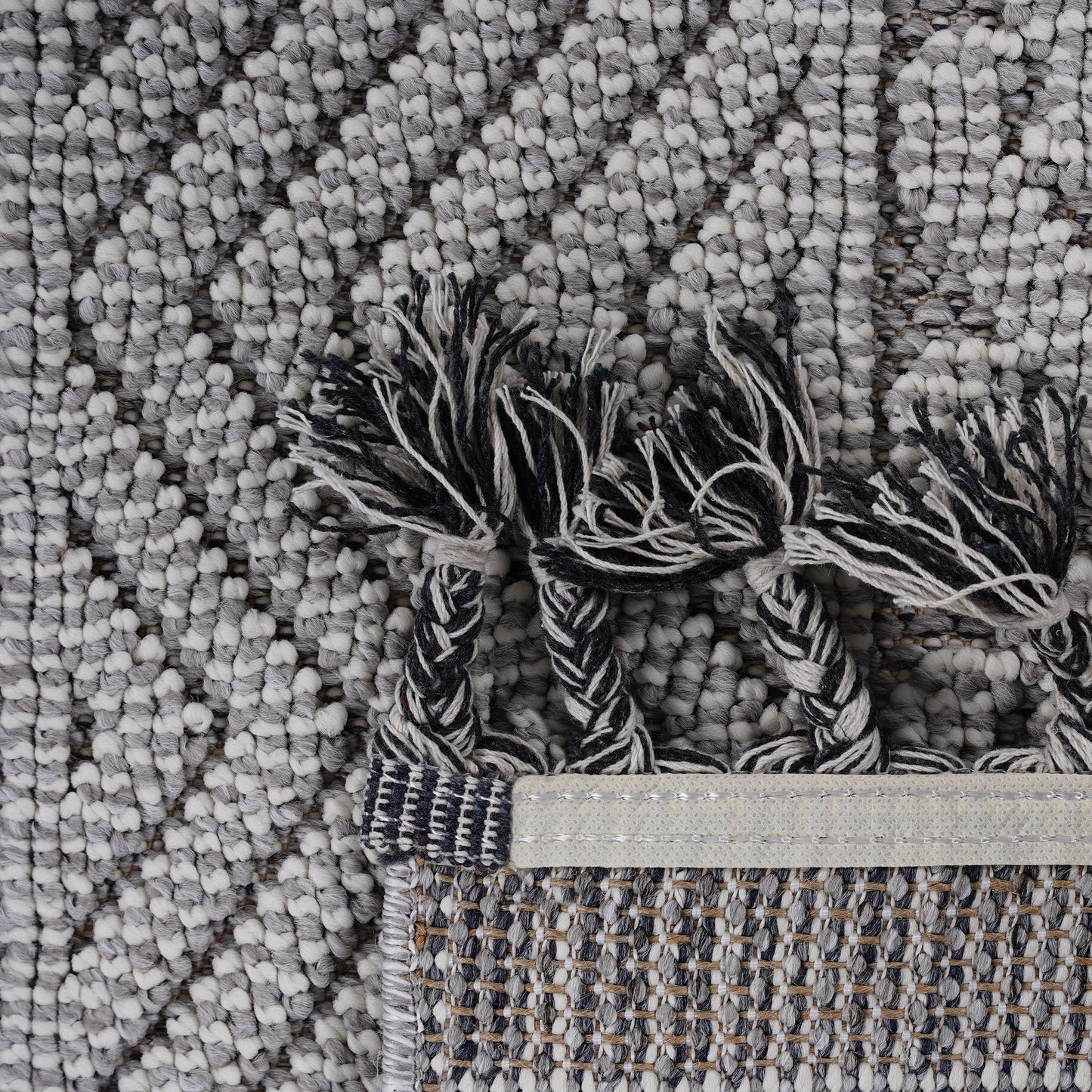 Close up of a textured grey and white geometric pattern rug with black and white braided tassels
