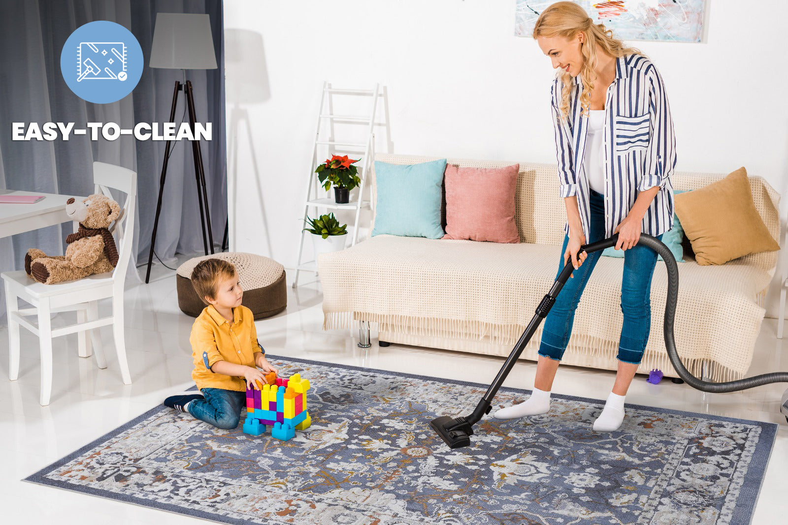 Woman vacuums a blue distressed floral pattern area rug in a living room setting