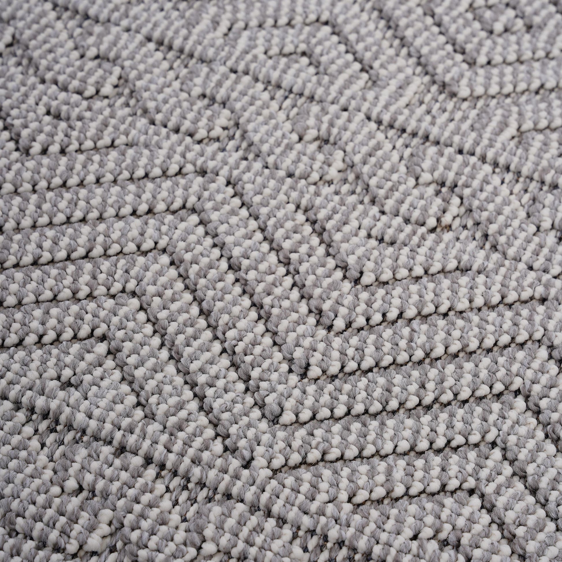 Closeup of textured grey and white woven rug with a geometric chevron pattern