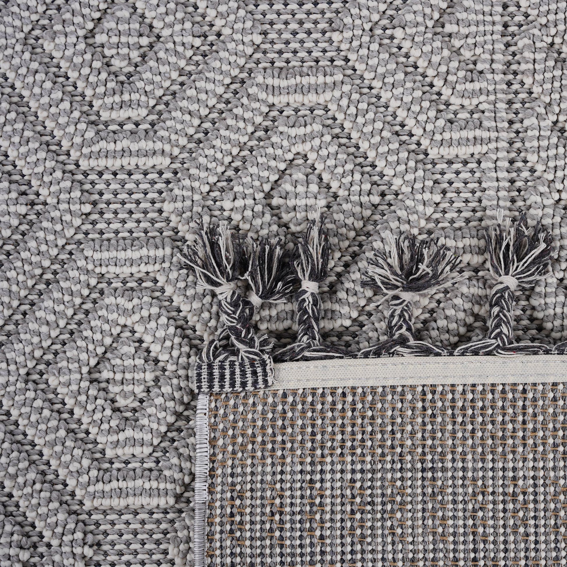 Closeup of a textured grey and white geometric weave area rug with braided tassels