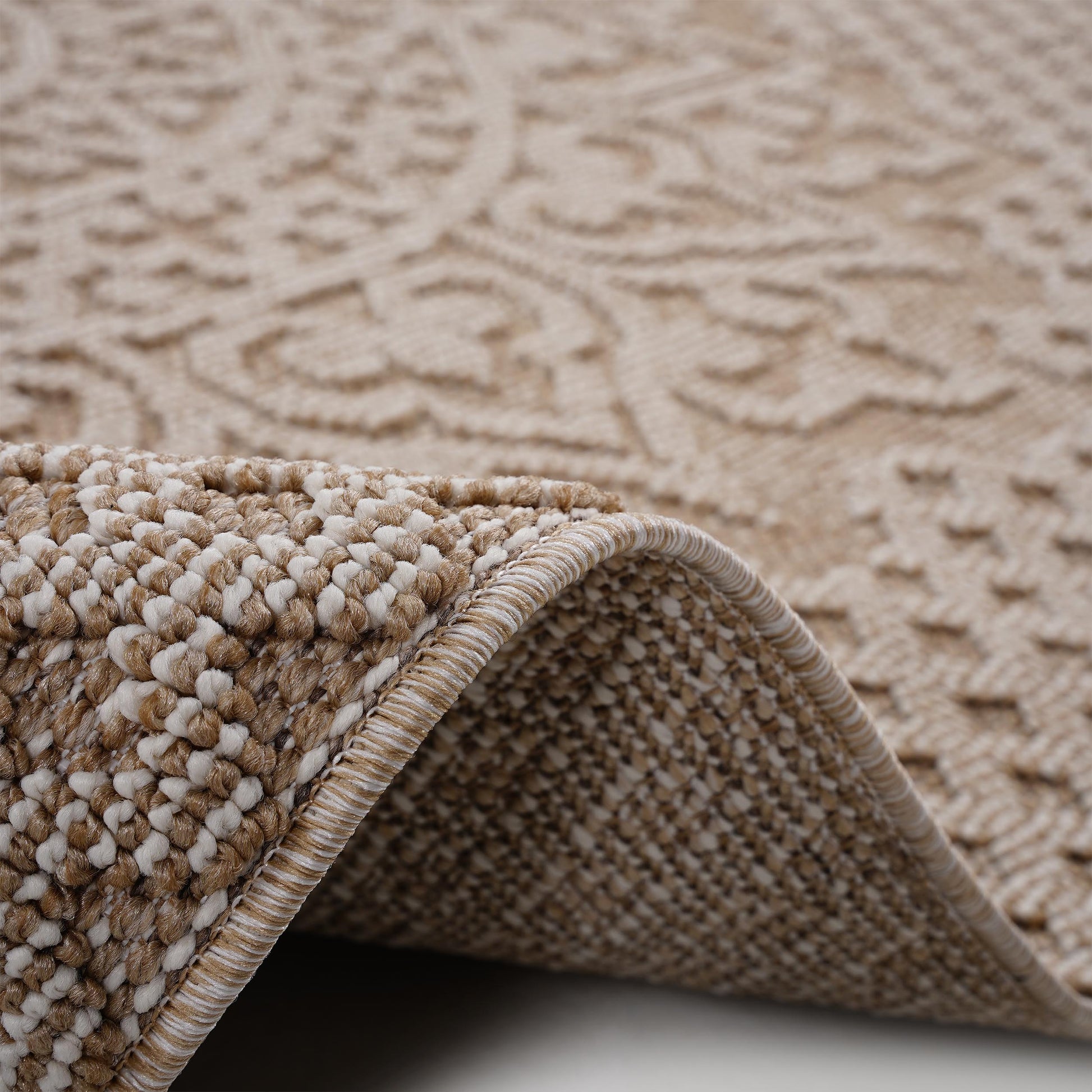 Closeup of a beige woven rug with a detailed textured pattern and rolled edge