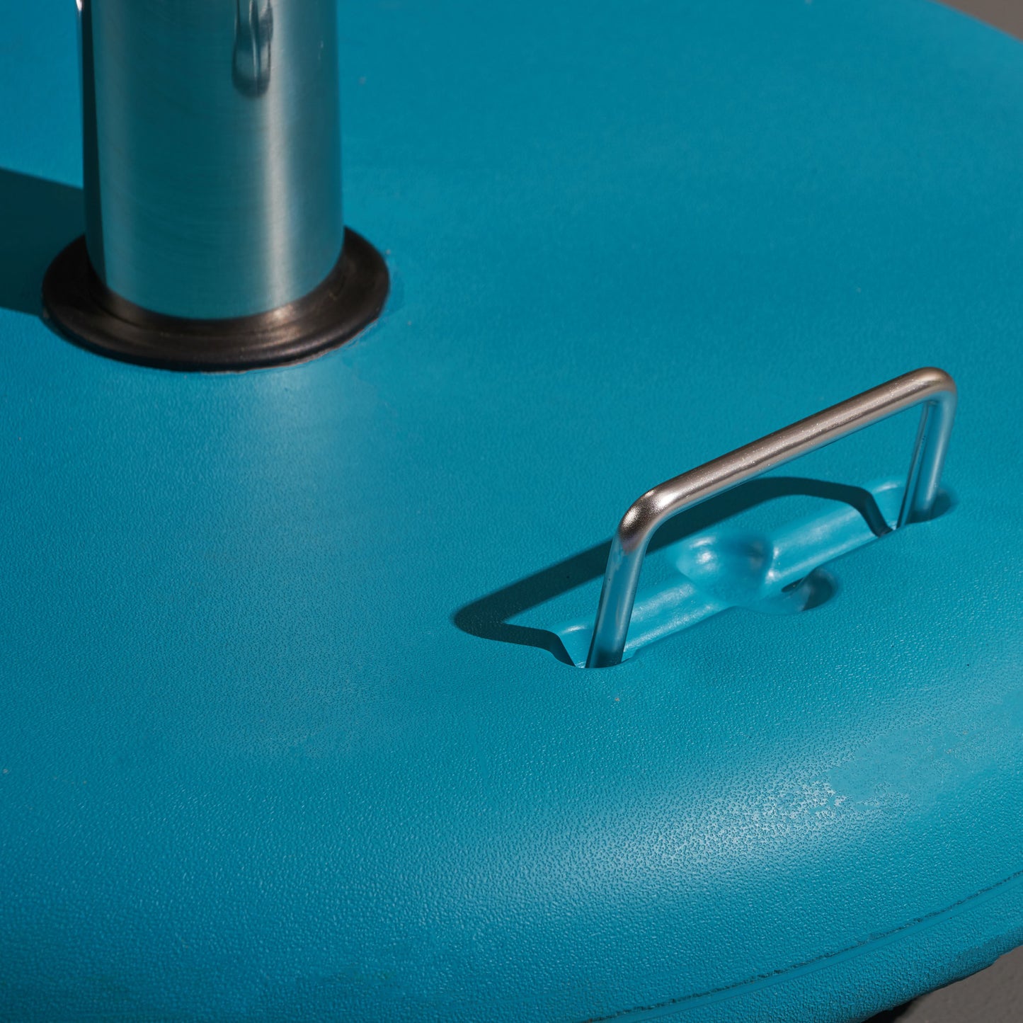 Closeup of a teal umbrella base with a silver handle outdoor use