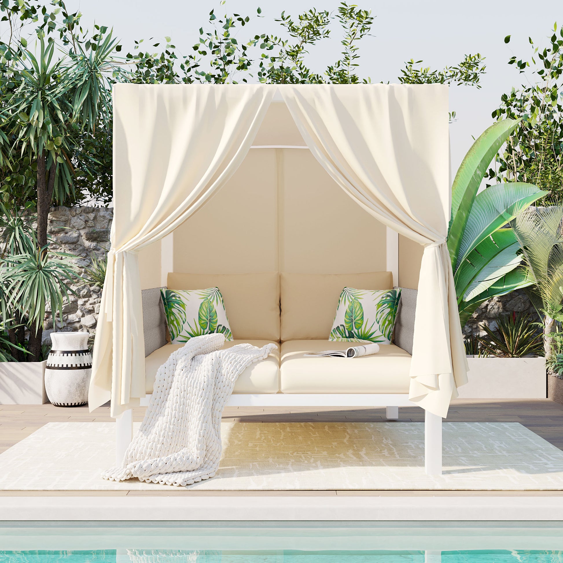 Cream canopy daybed with tropical leaf cushions and a chunky knit throw perfect for poolside lounging