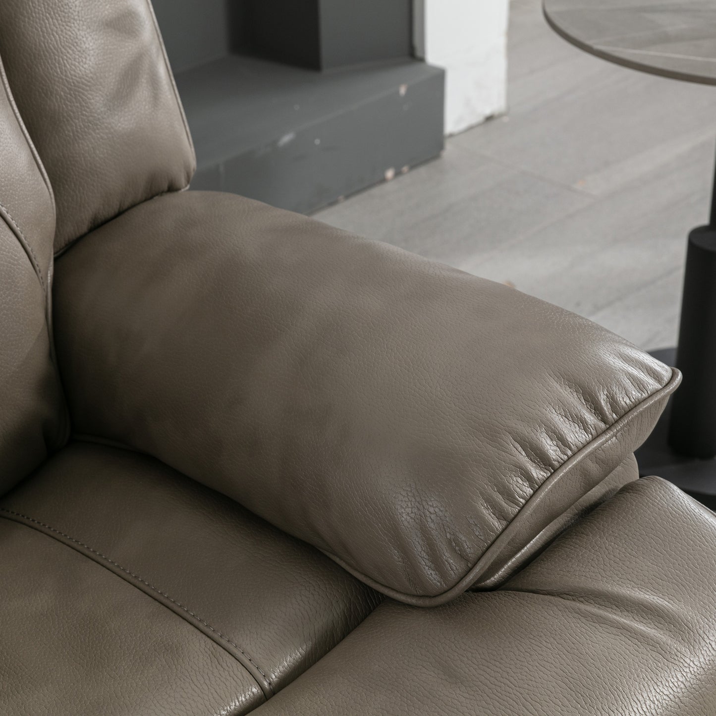 Closeup of a taupe leather recliner armrest with detailed stitching and a plush cushion