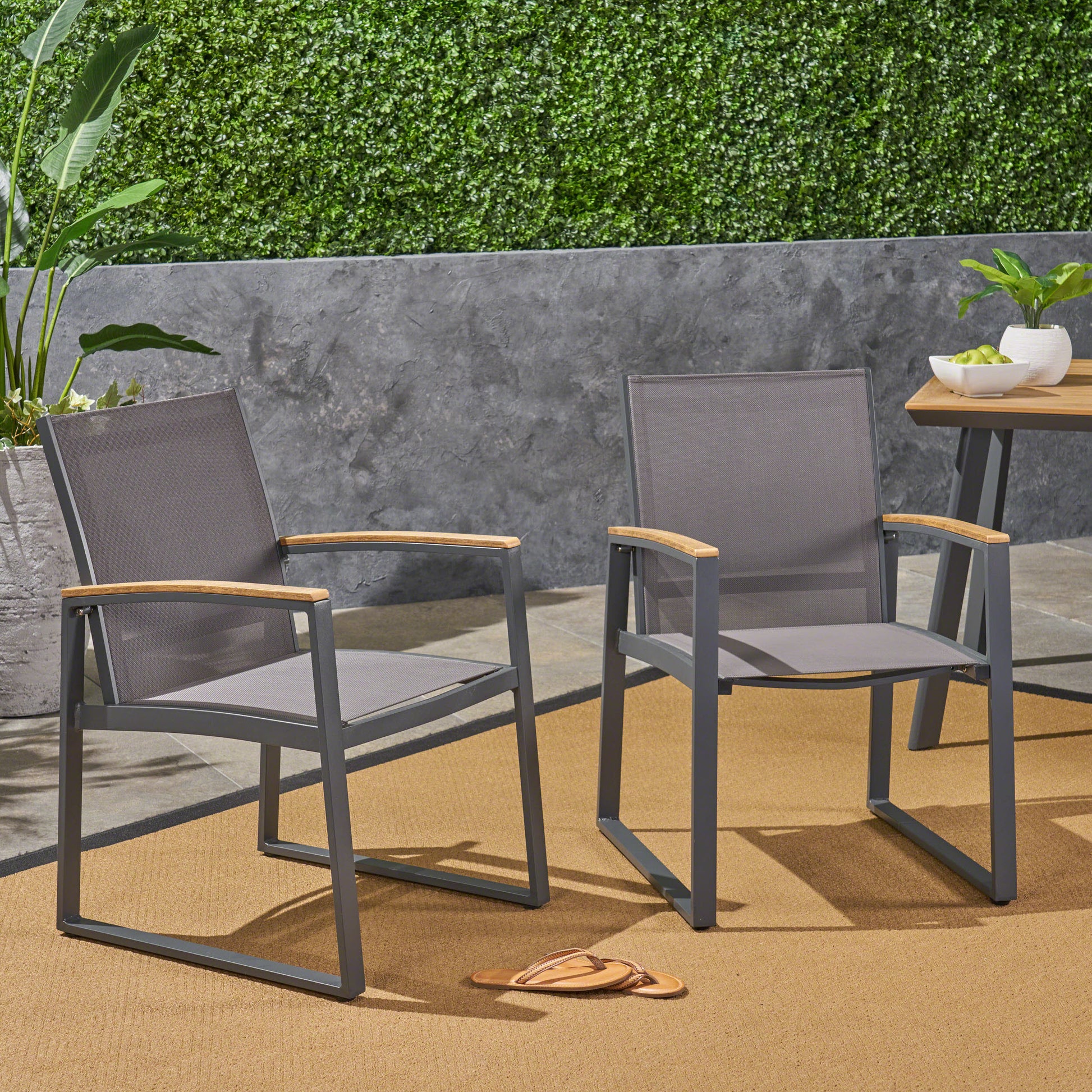 Two grey mesh outdoor dining chairs with wooden armrests on a woven rug