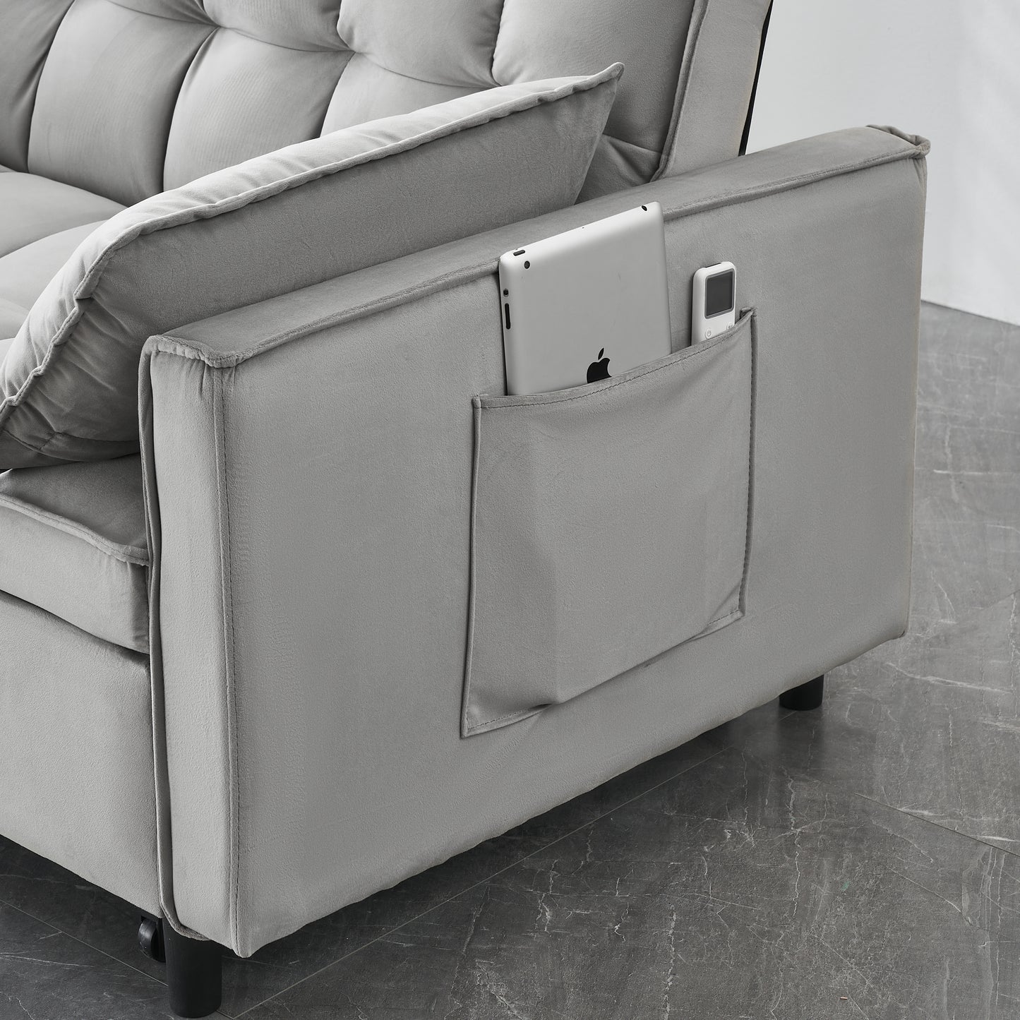 Gray velvet sofa with convenient side pocket holding a tablet and remote