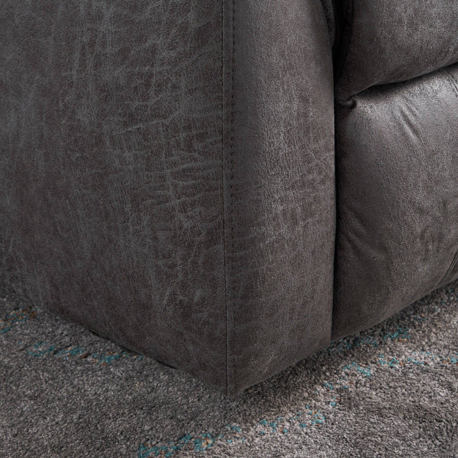 Dark grey faux leather corner of a plush armchair showing stitched seams and textured finish