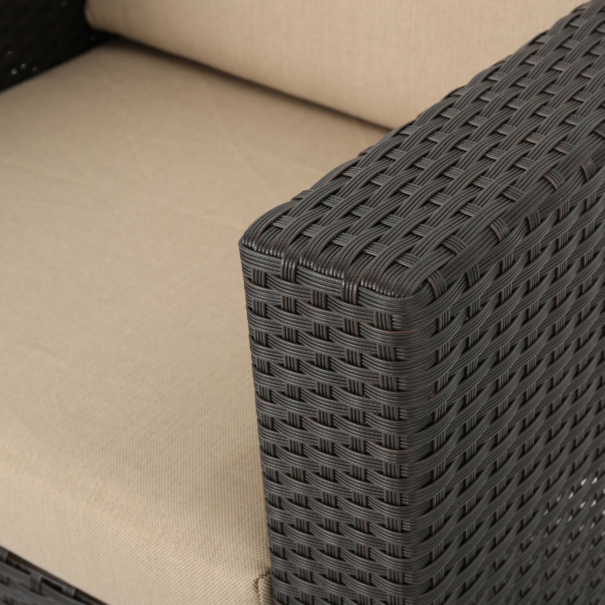 Close up of a dark brown rattan armchair armrest with a beige cushion