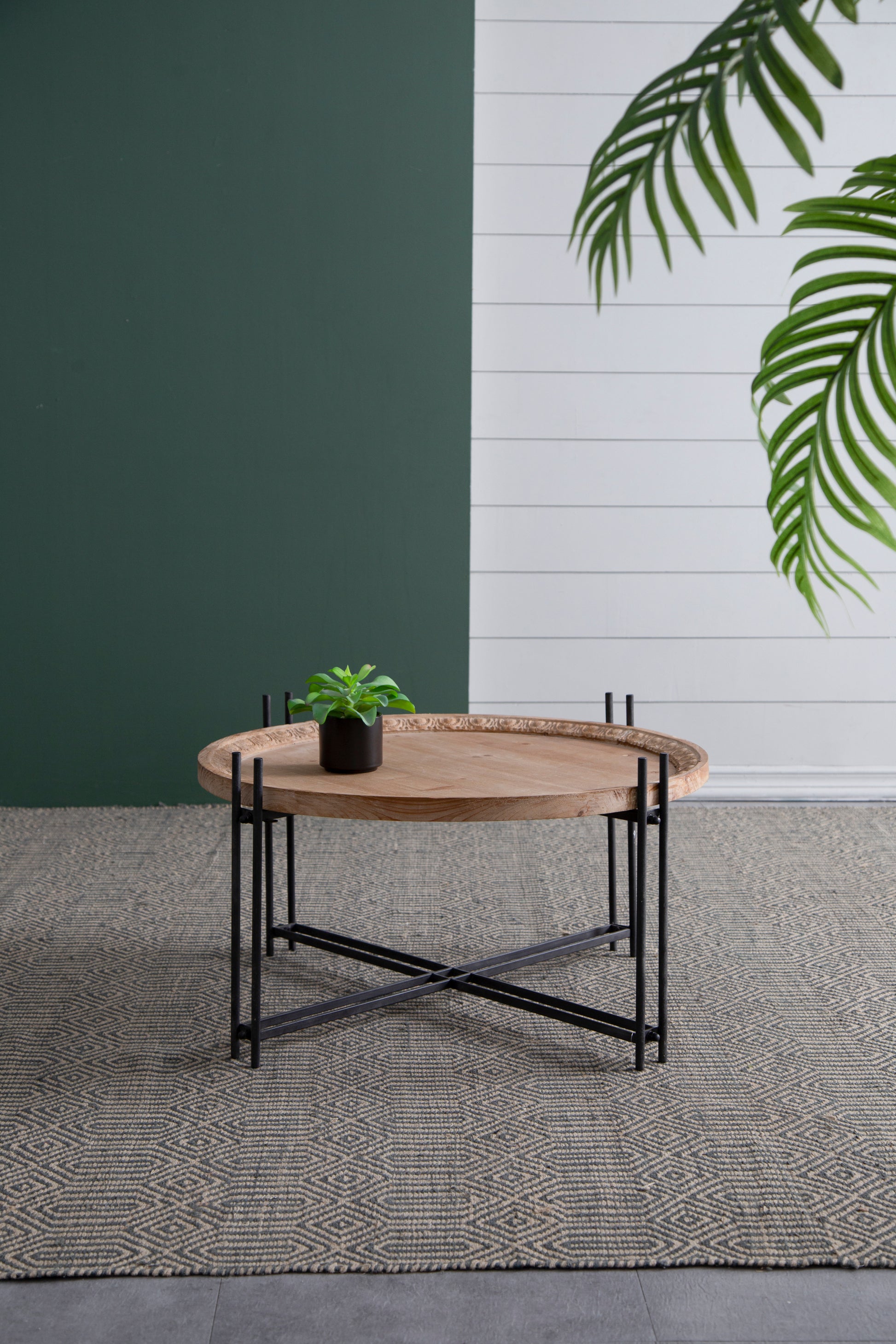 Round wooden tray coffee table with black metal legs and carved edge detail