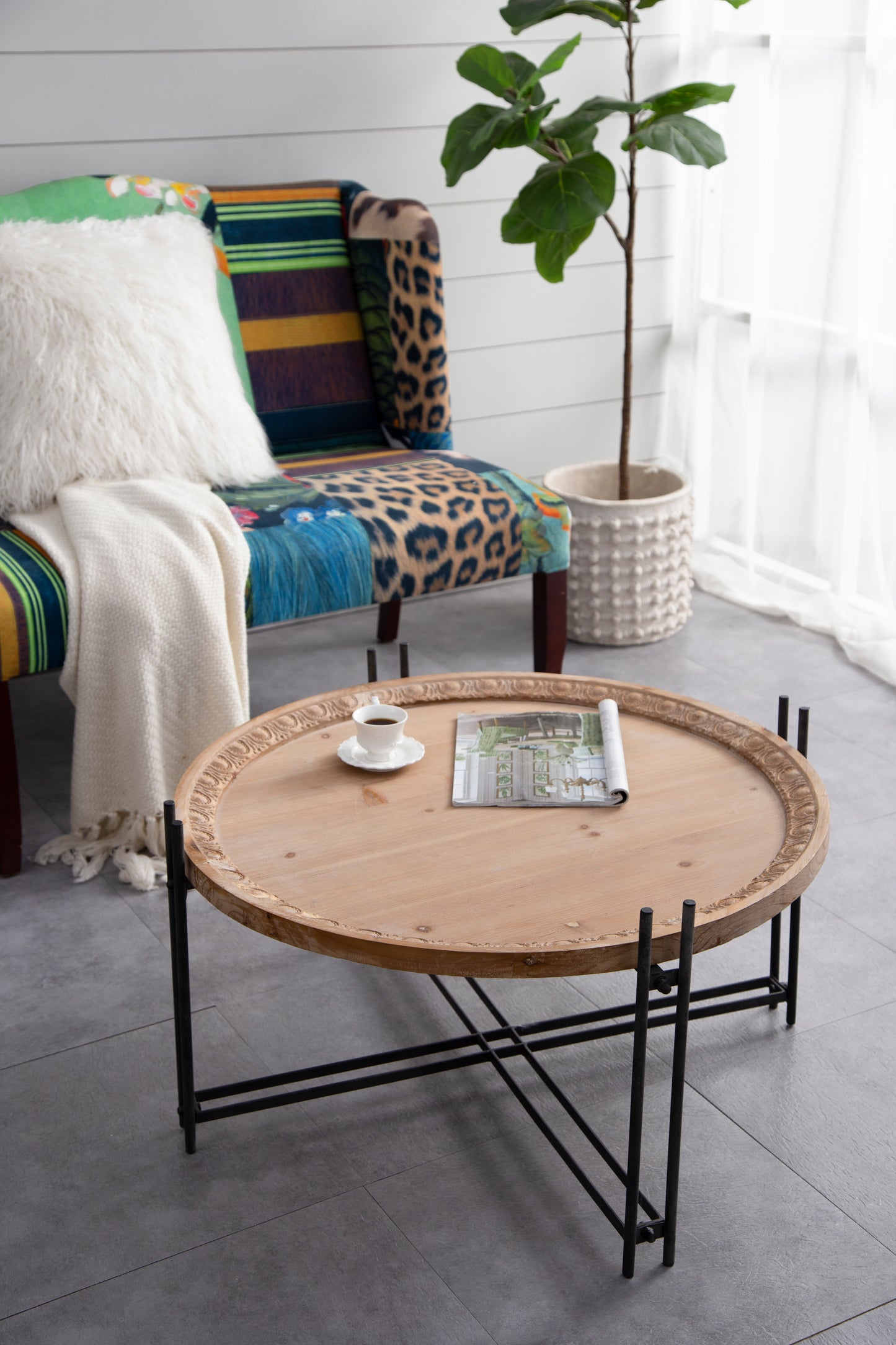 Round distressed wood coffee table with ornate carved edge and black metal legs