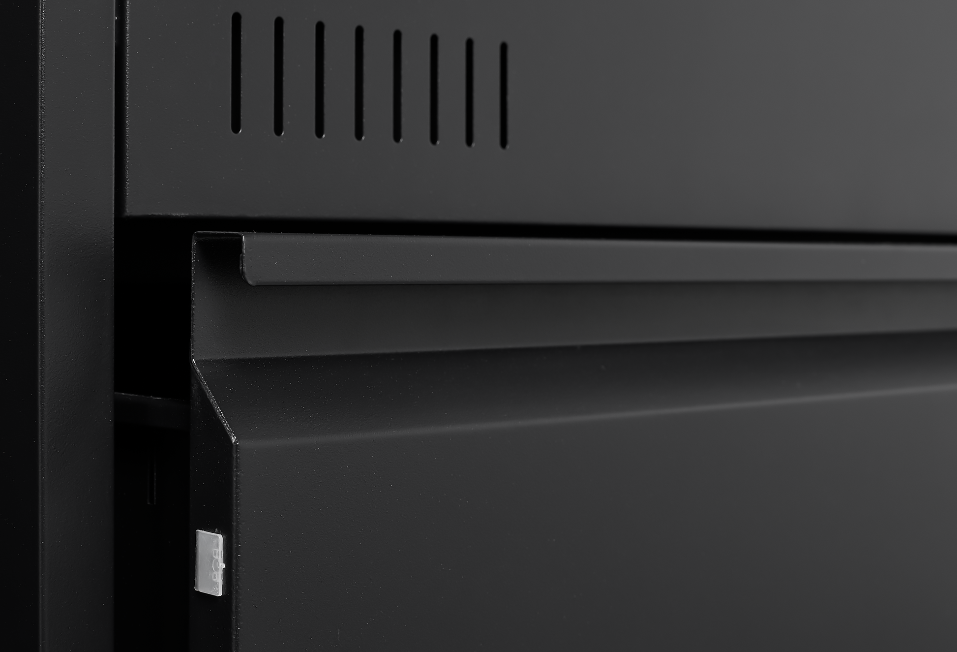 Black metal cabinet with vent slits and a partially open drawer for storage
