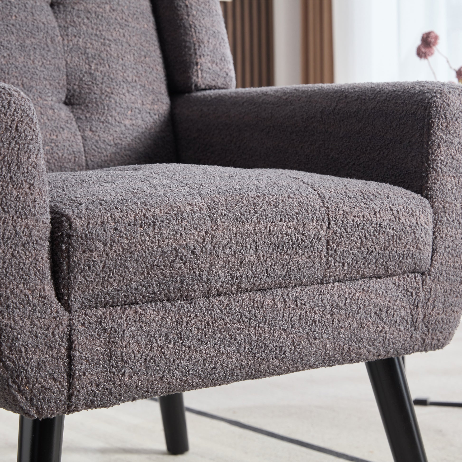 Closeup of a textured grey boucl armchair with button tufting and black legs