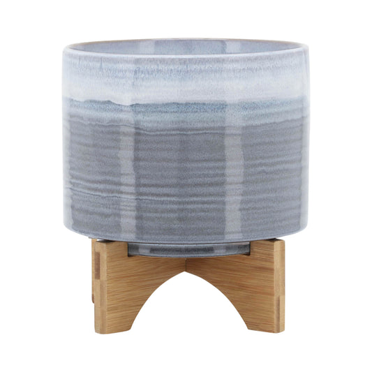 Glazed ceramic planter with bluegray gradient supported by a wooden stand for indoor plants