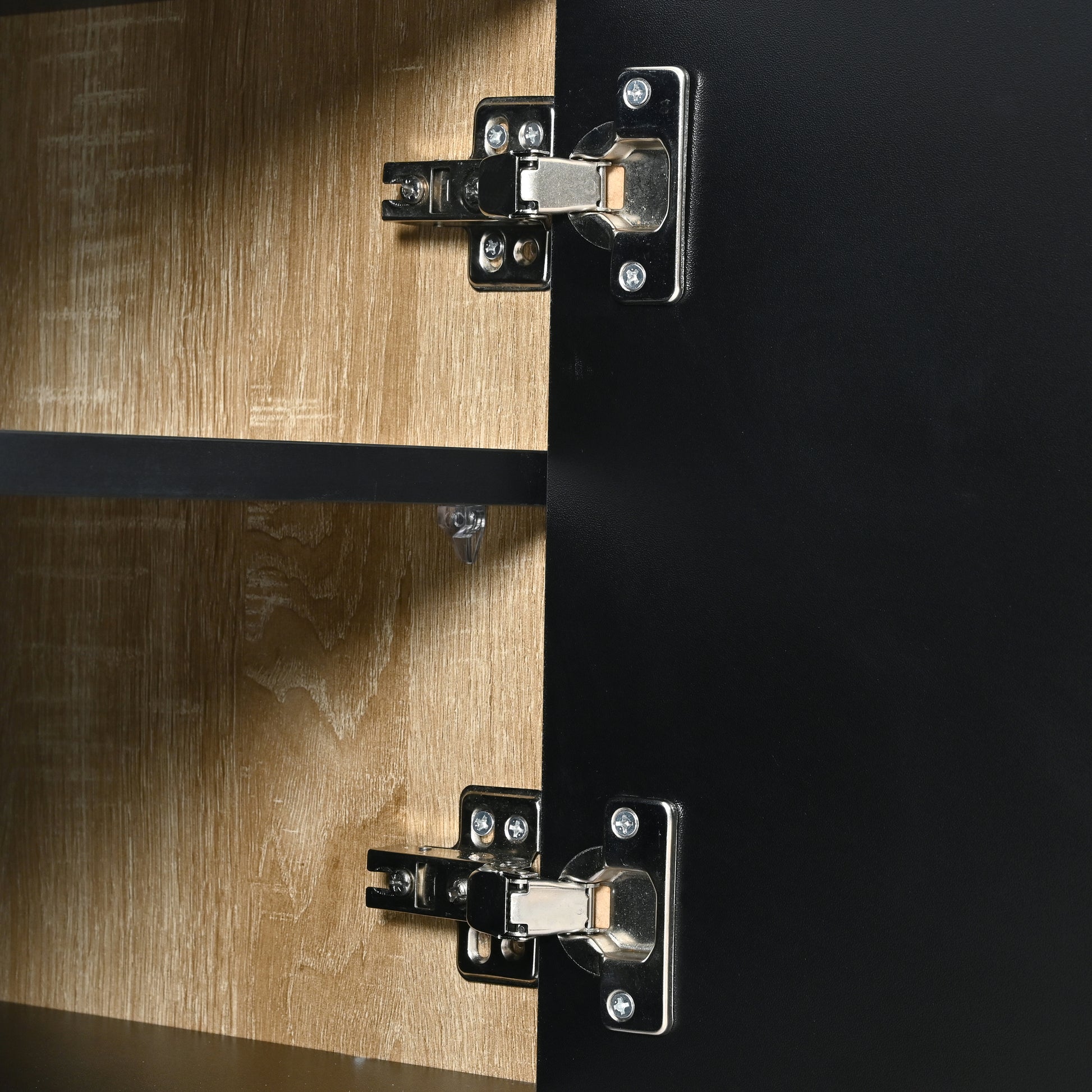Closeup of two silver cabinet door hinges on black and wood grain panels